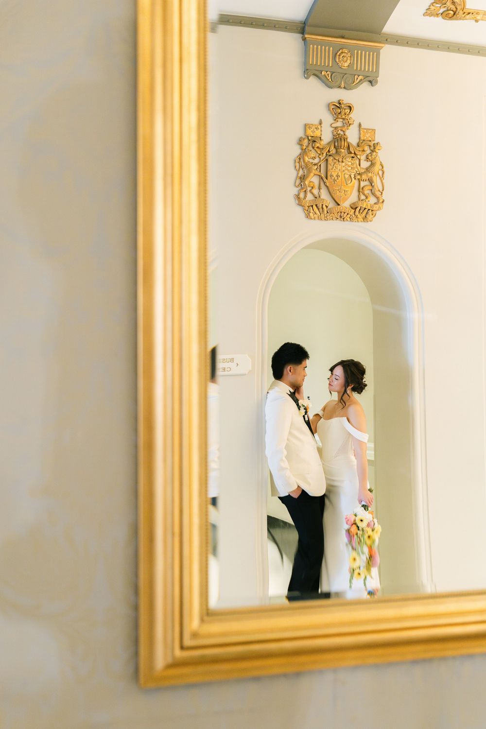 bride and groom reflected in a gold-framed mirror during a classic wedding portrait