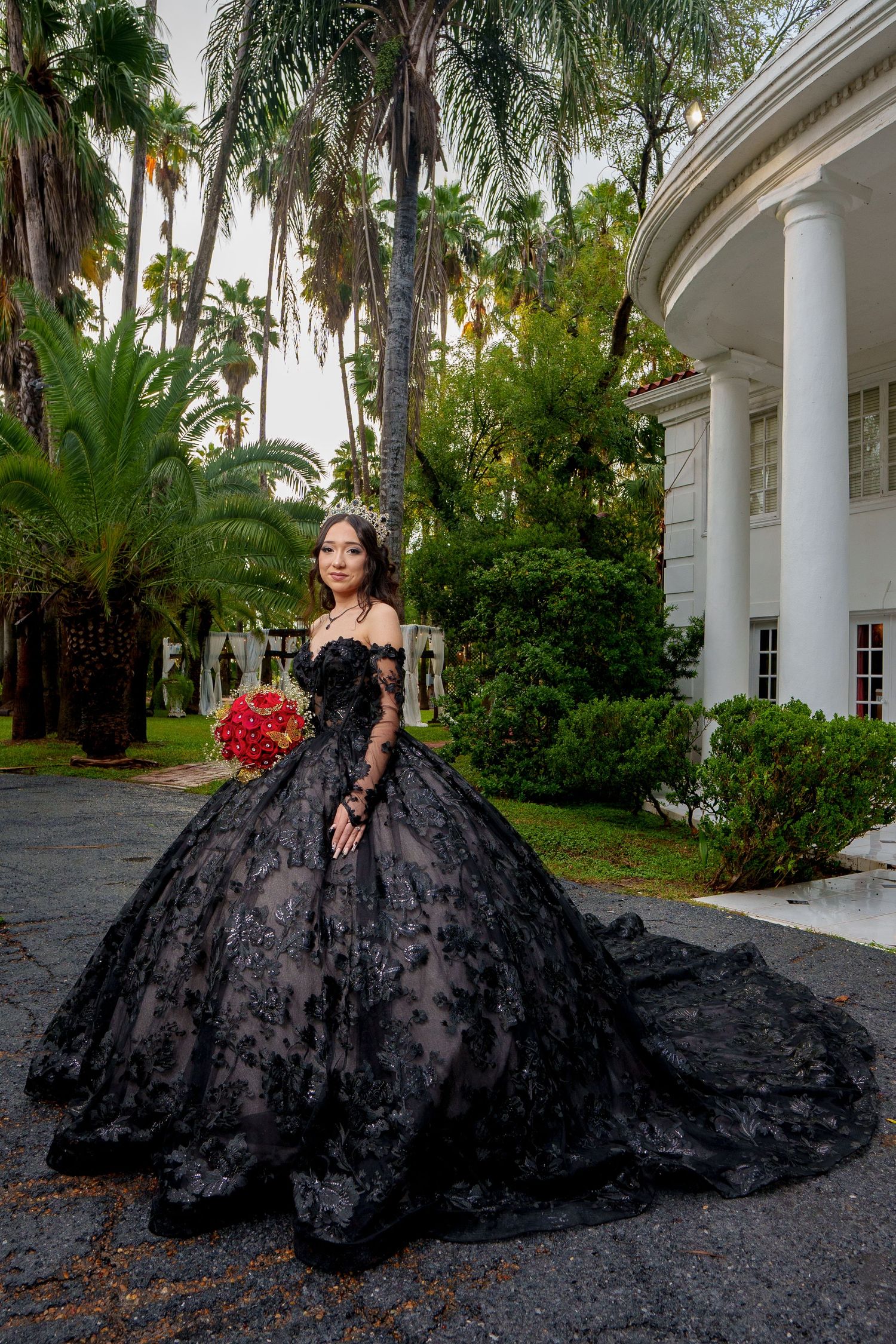 A dramatic black ball gown with lace details photographed in front of a white columned mansion.