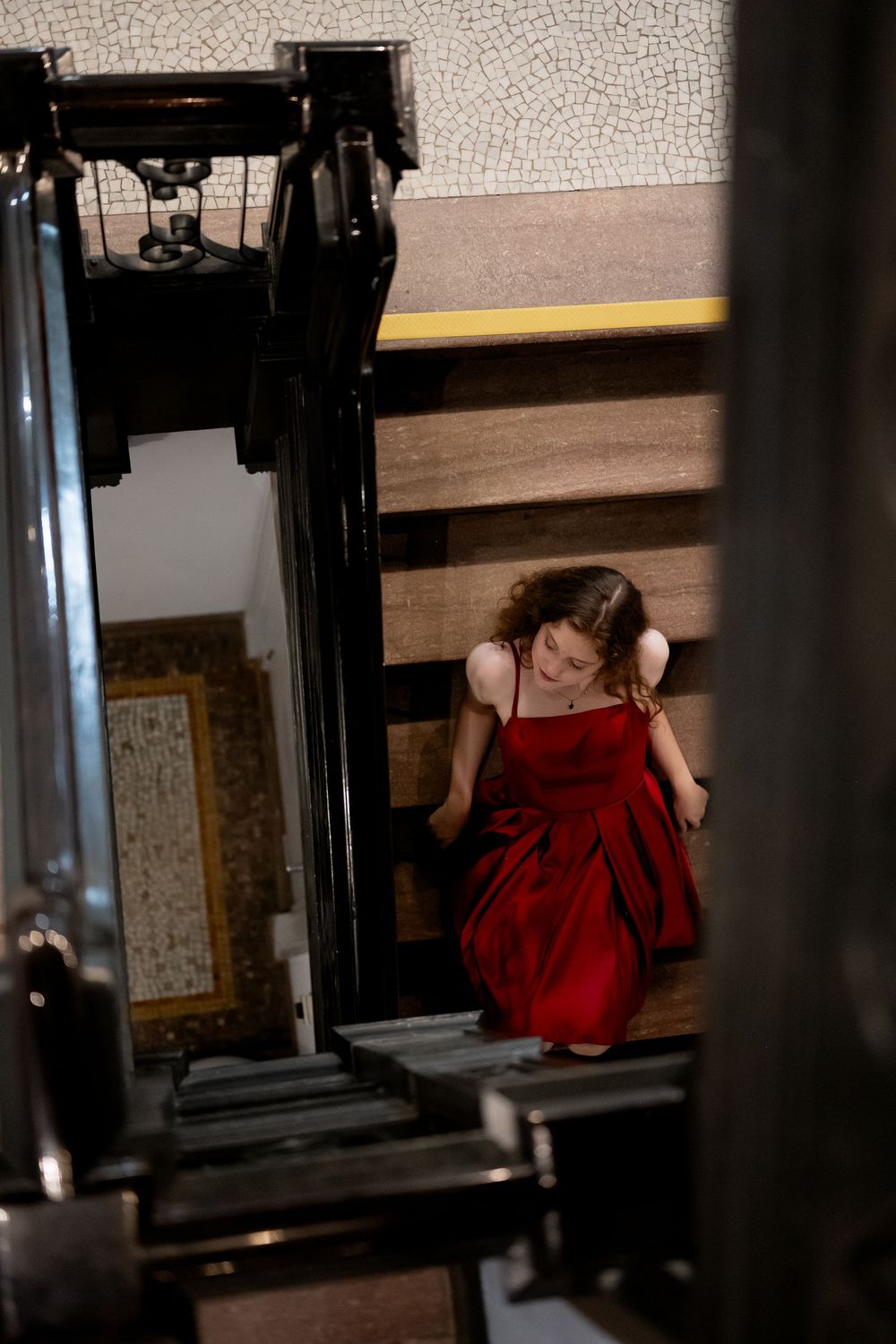 A person in a red dress descends a dark wooden staircase, captured through the frame of exercise equipment.