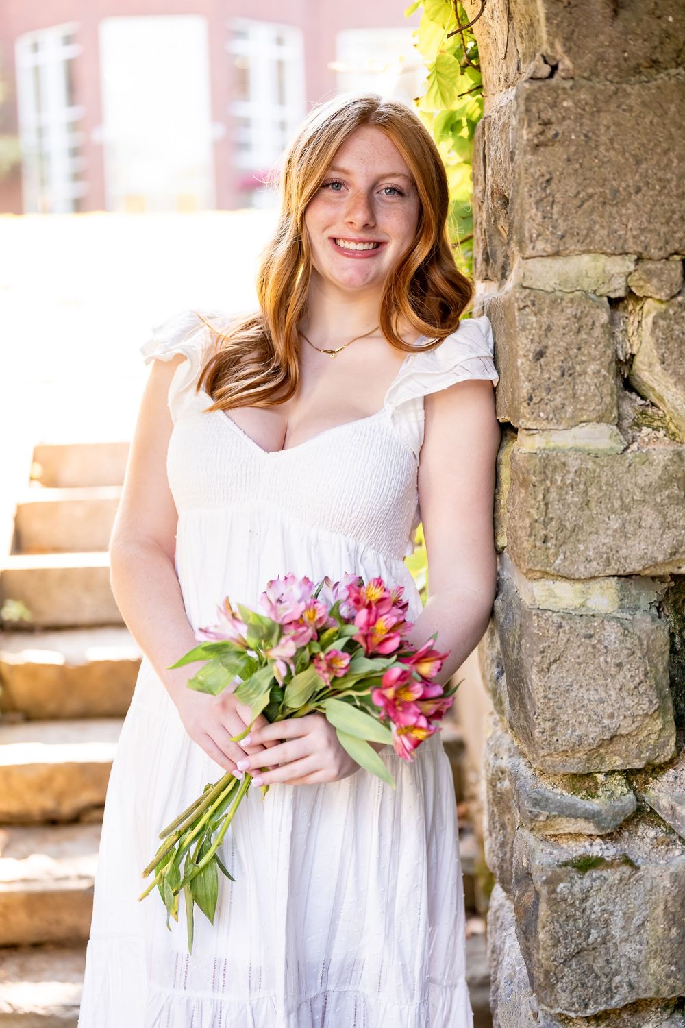 A person in a white dress holds a bouquet of pink tulips against a stone wall background.
