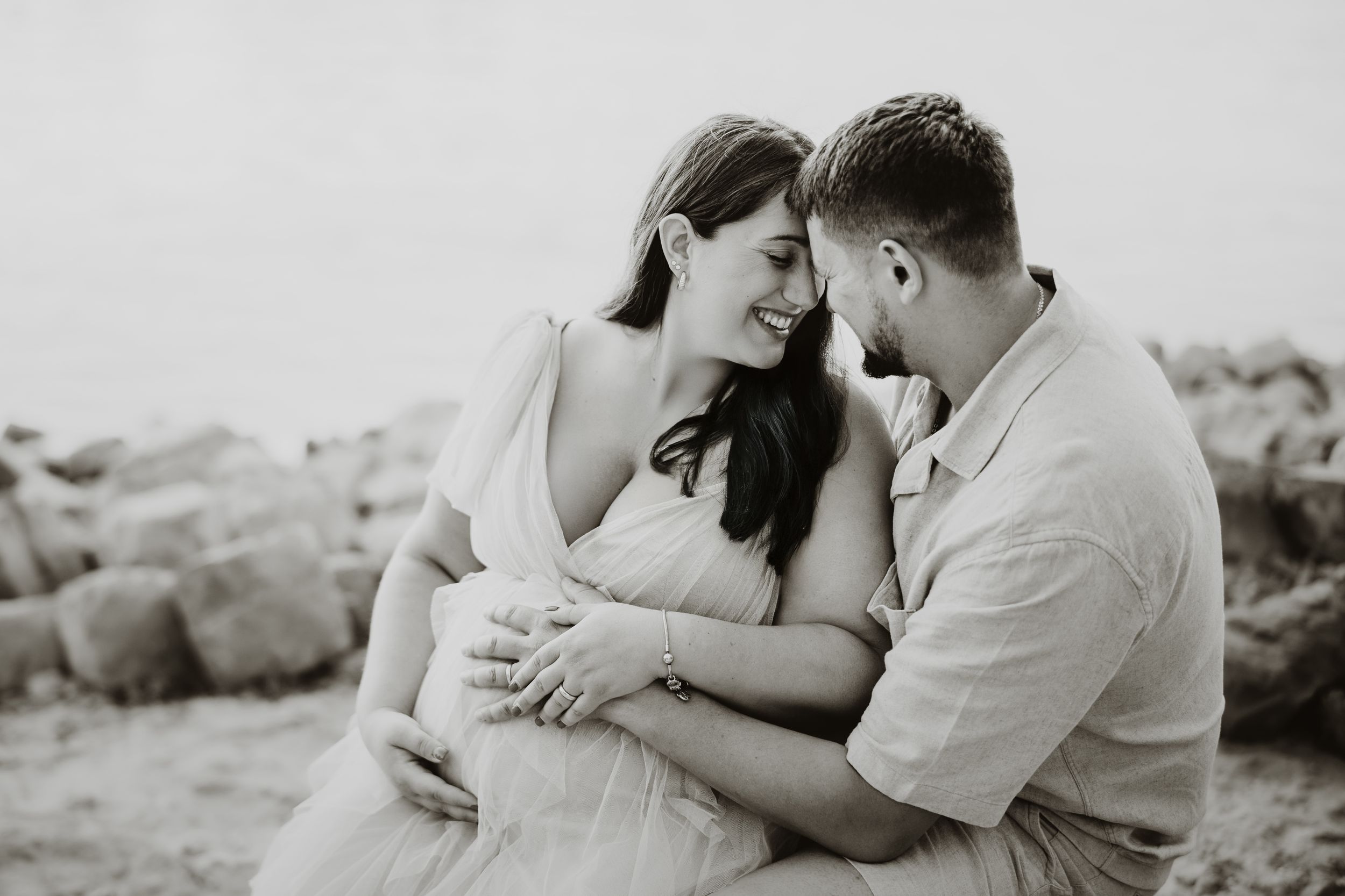Romantic couple embracing on rocky beach during sunset photoshoot.