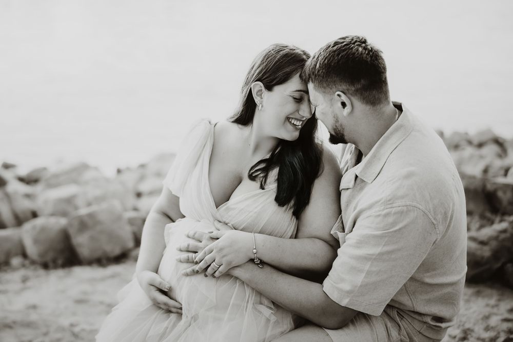 Romantic couple embracing on rocky beach during sunset photoshoot.