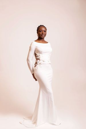 A pregnant woman in a white fitted dress poses elegantly against a light backdrop in a maternity photoshoot series.