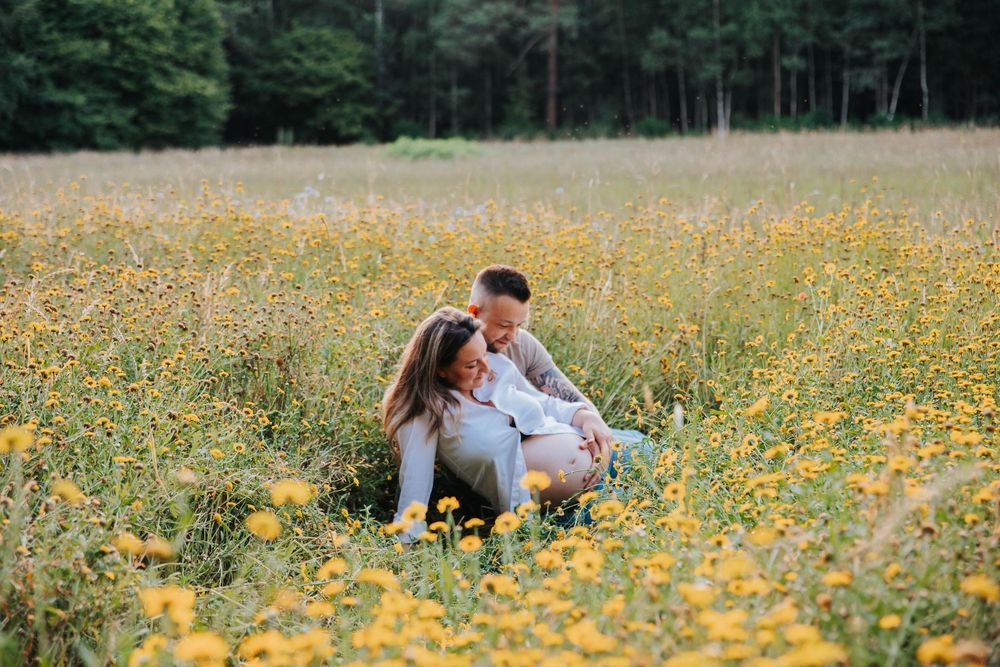 Couple sits lovingly in a vibrant meadow filled with yellow wildflowers on a summer day.