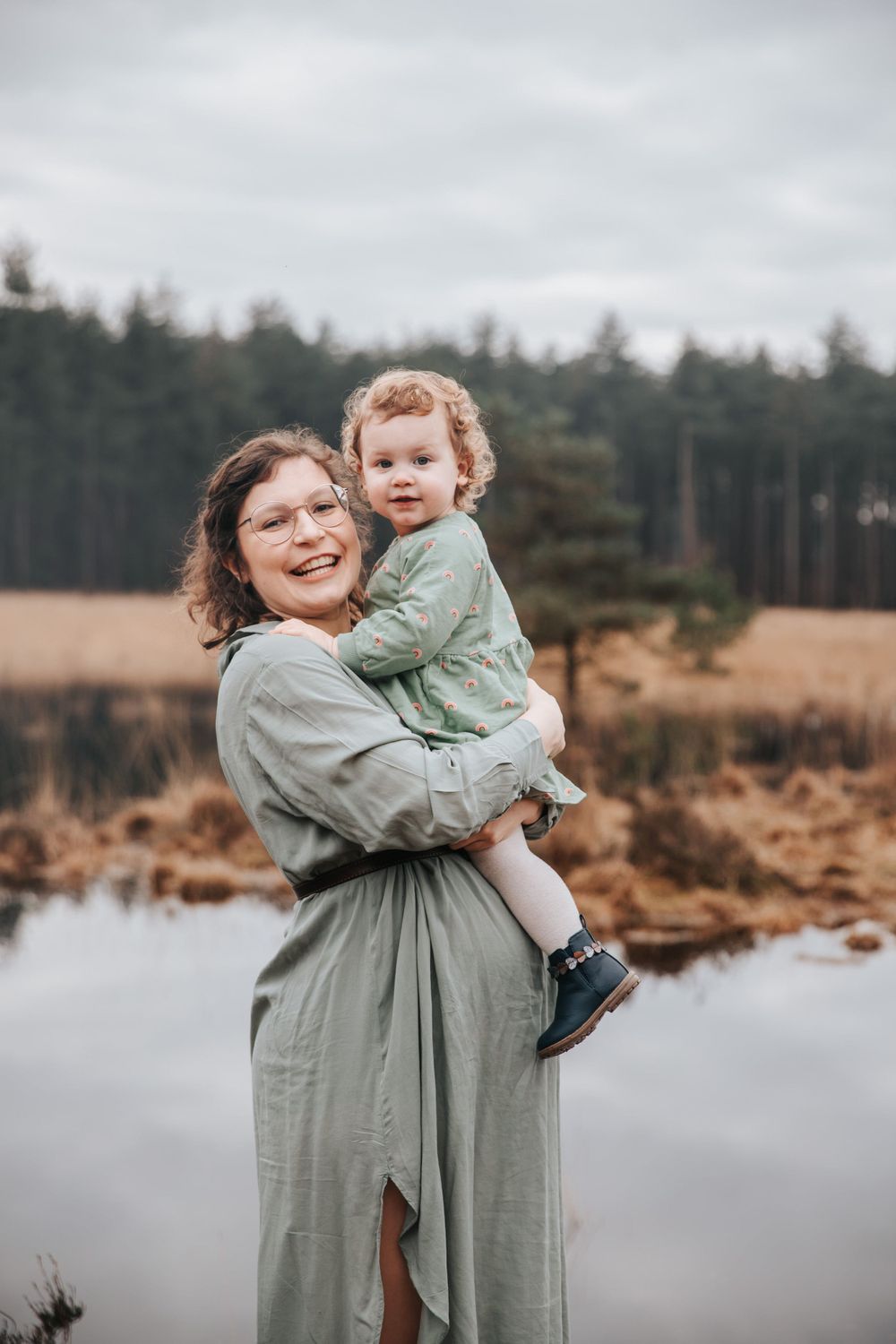 Outdoor portrait by lake with forest backdrop in autumn colors.