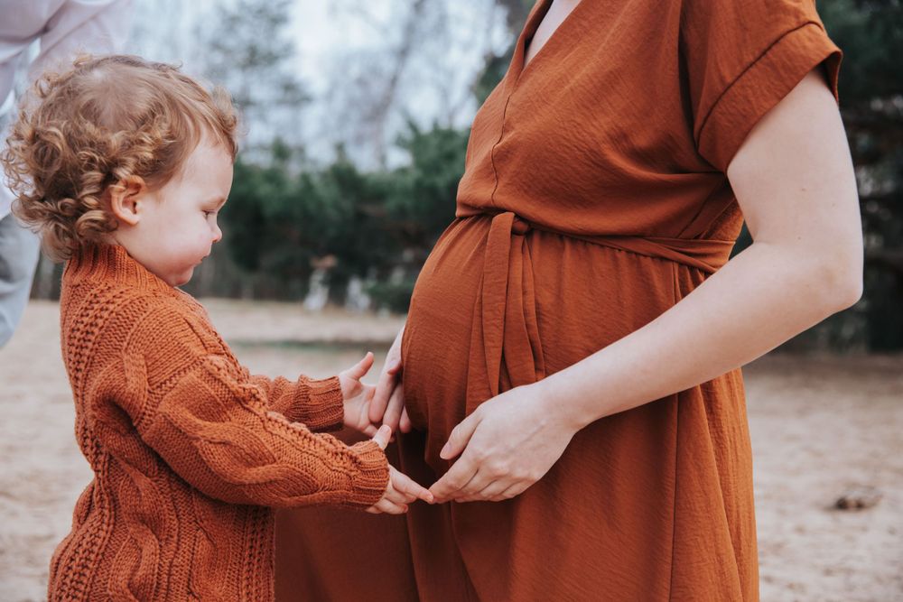 Toddler in orange sweater touching pregnant belly matching mother's dress.