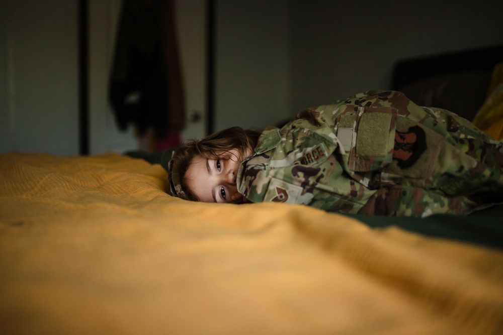 A person in military camouflage uniform lies sleeping on a tan colored bed.
