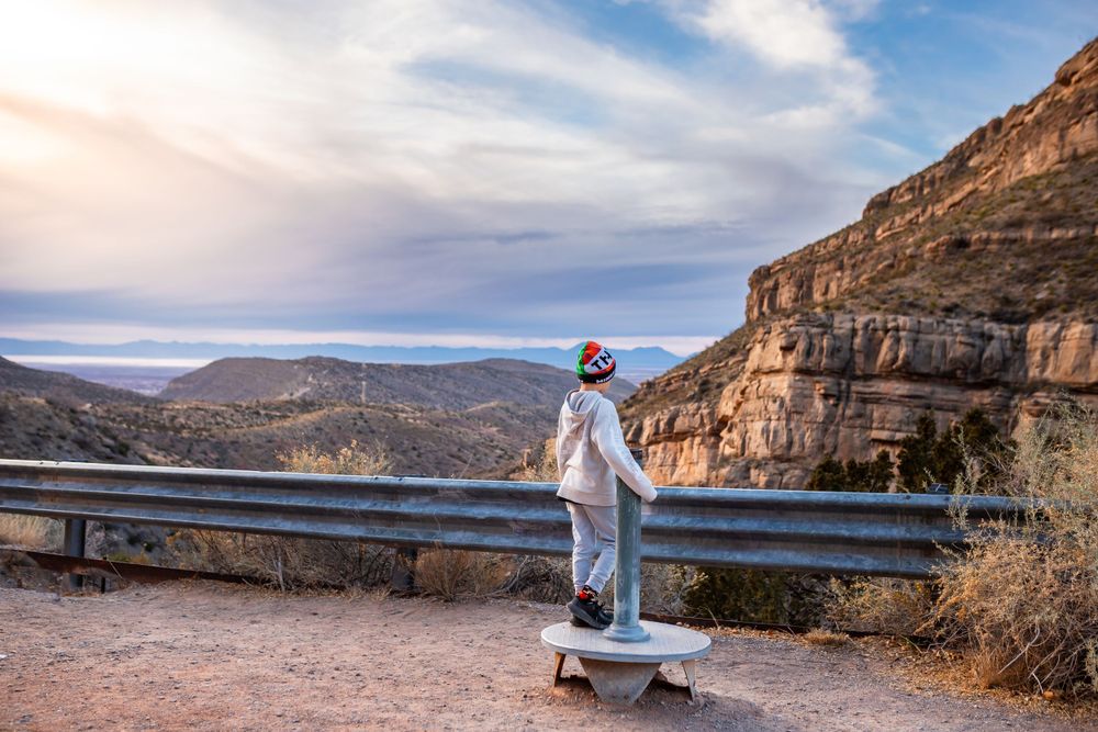 A couple in wedding attire stands along a scenic mountain road overlooking a dramatic desert canyon landscape.