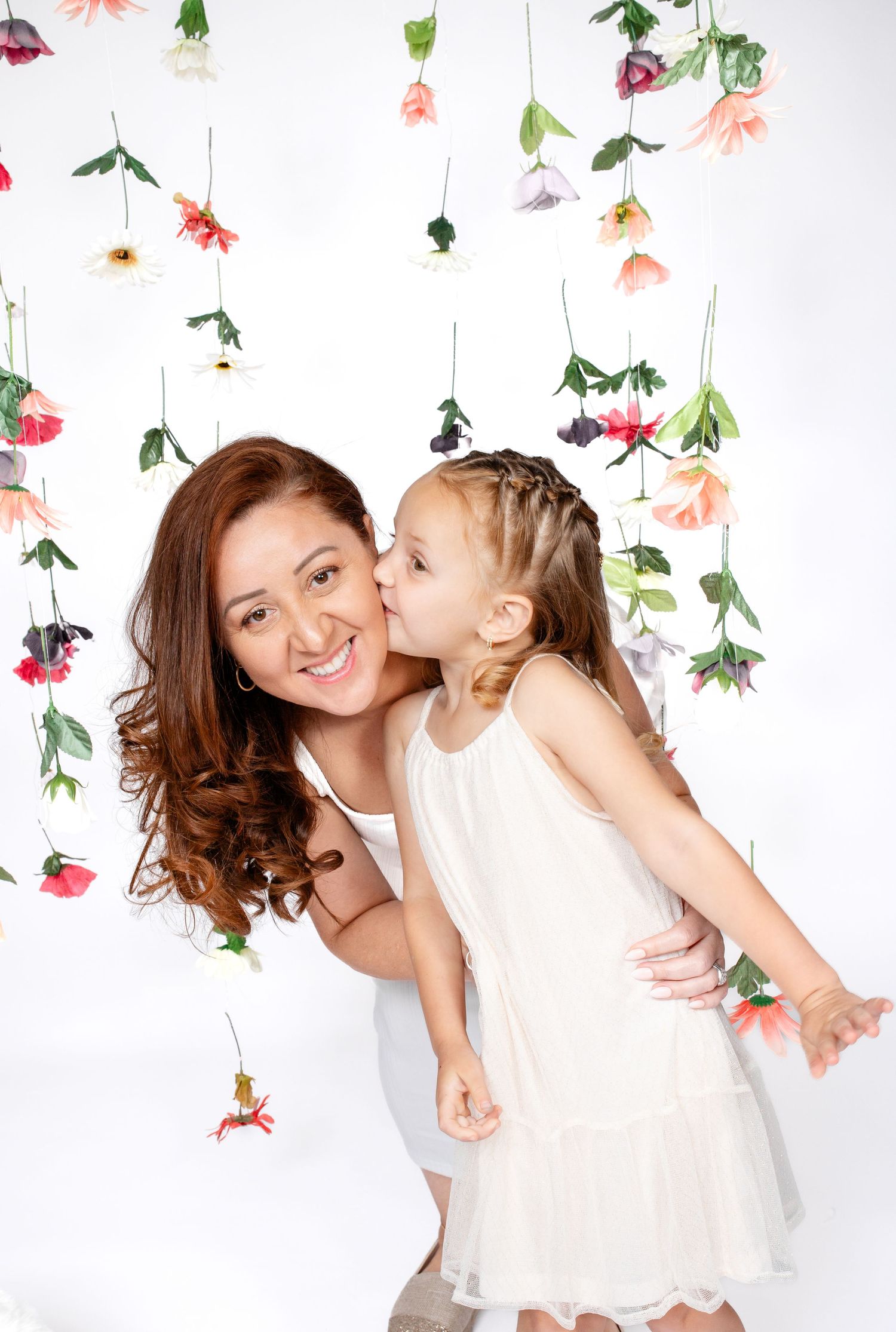 A sweet moment captured against a backdrop of hanging floral decorations in pink and peach tones.