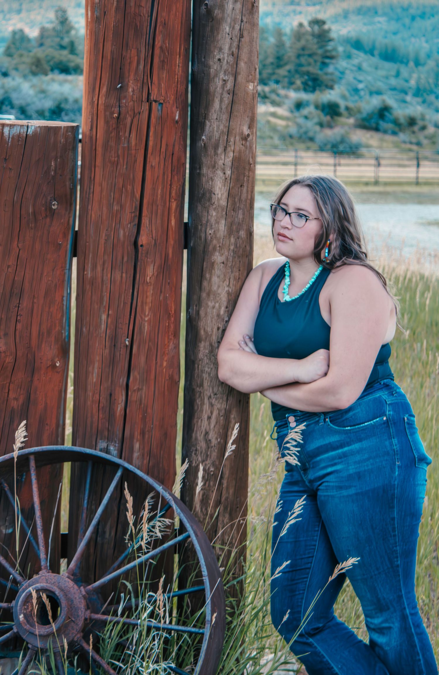 Portrait against rustic wooden fence with vintage wagon wheel in rural setting.