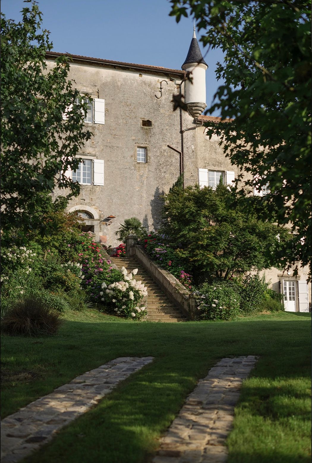 Stone castle exterior with winding stone pathway through a lush green lawn leading to elevated entrance stairs.