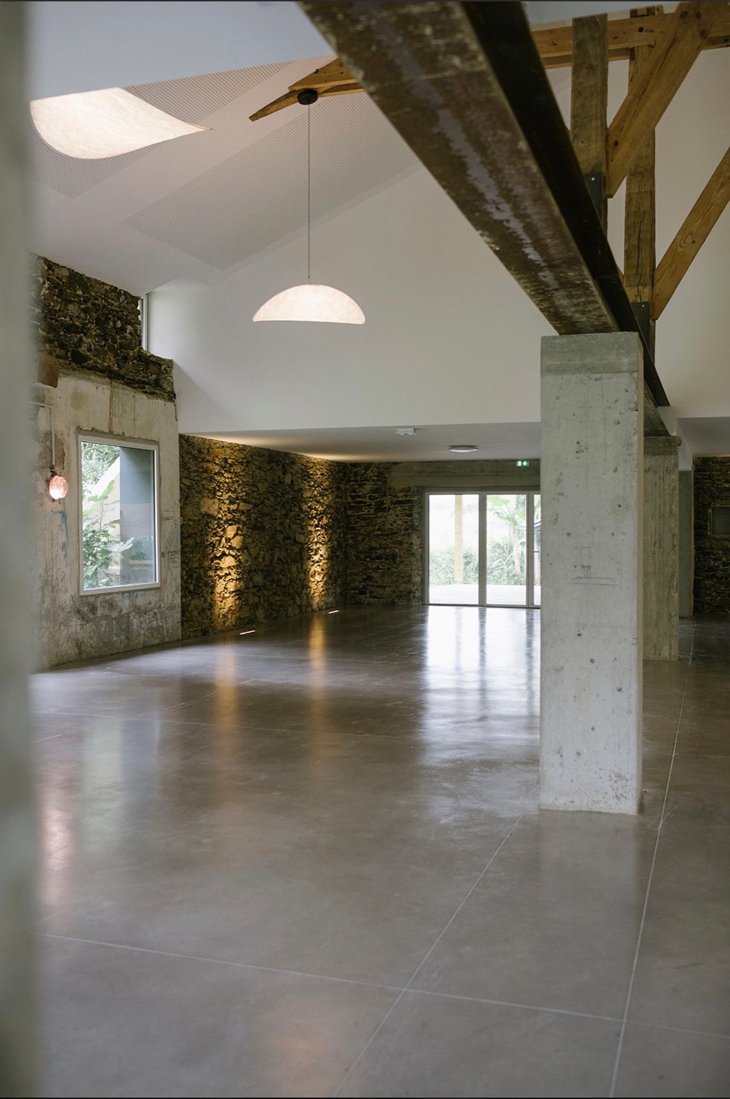 Modern interior space with exposed stone walls, wooden beams, and polished concrete floors in an open floor plan layout.