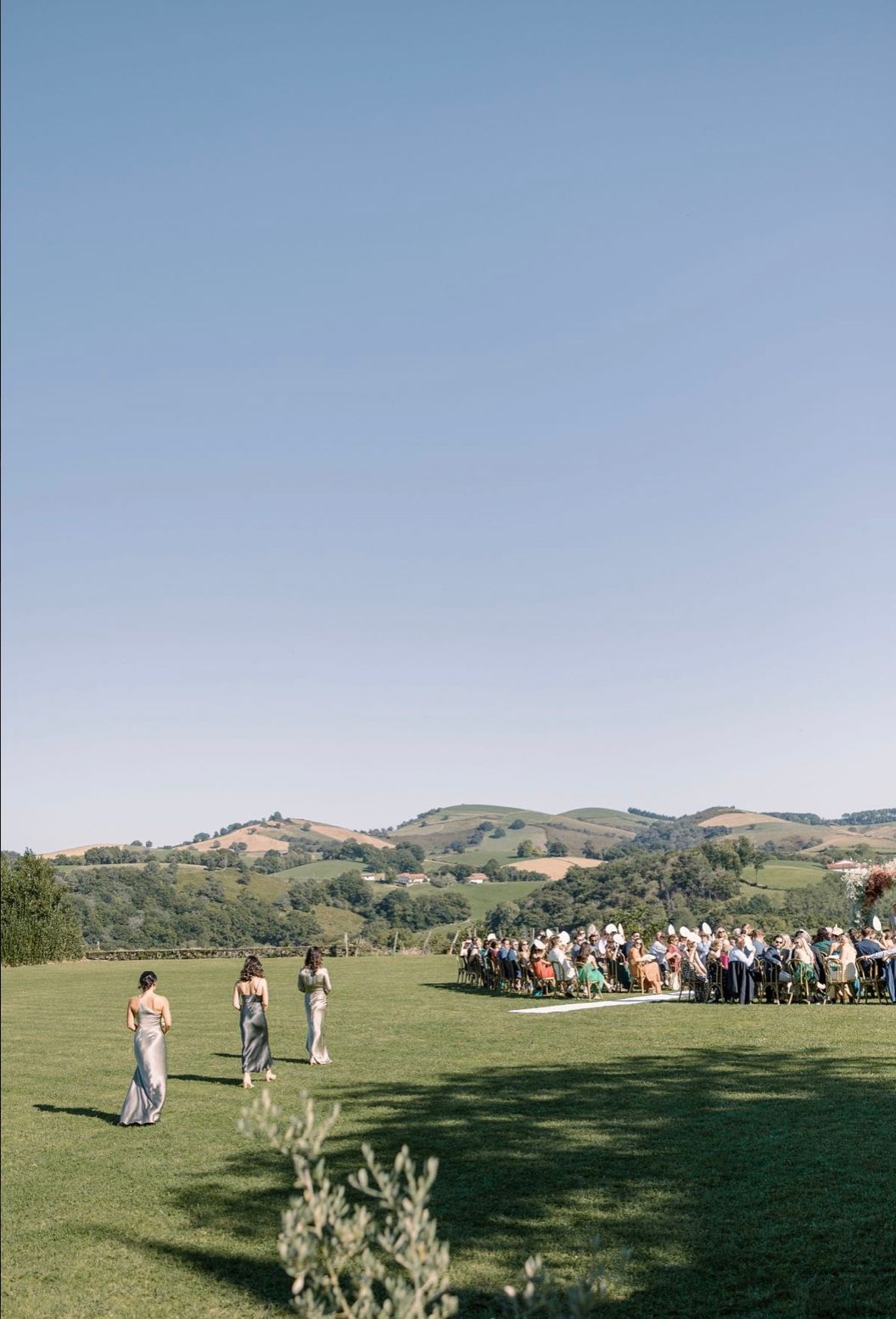 A panoramic view of wedding guests gathered on a rolling green hillside during an outdoor ceremony.