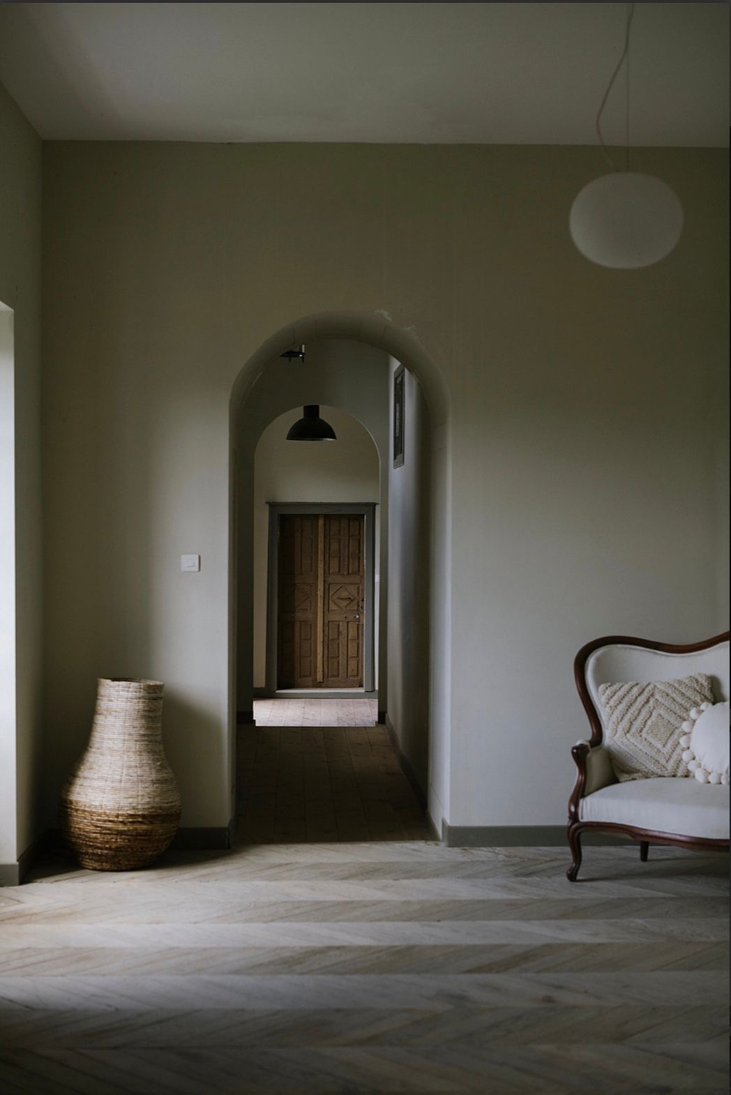 A minimalist interior space with arched doorways, woven baskets, and a chaise lounge creating a serene atmosphere.