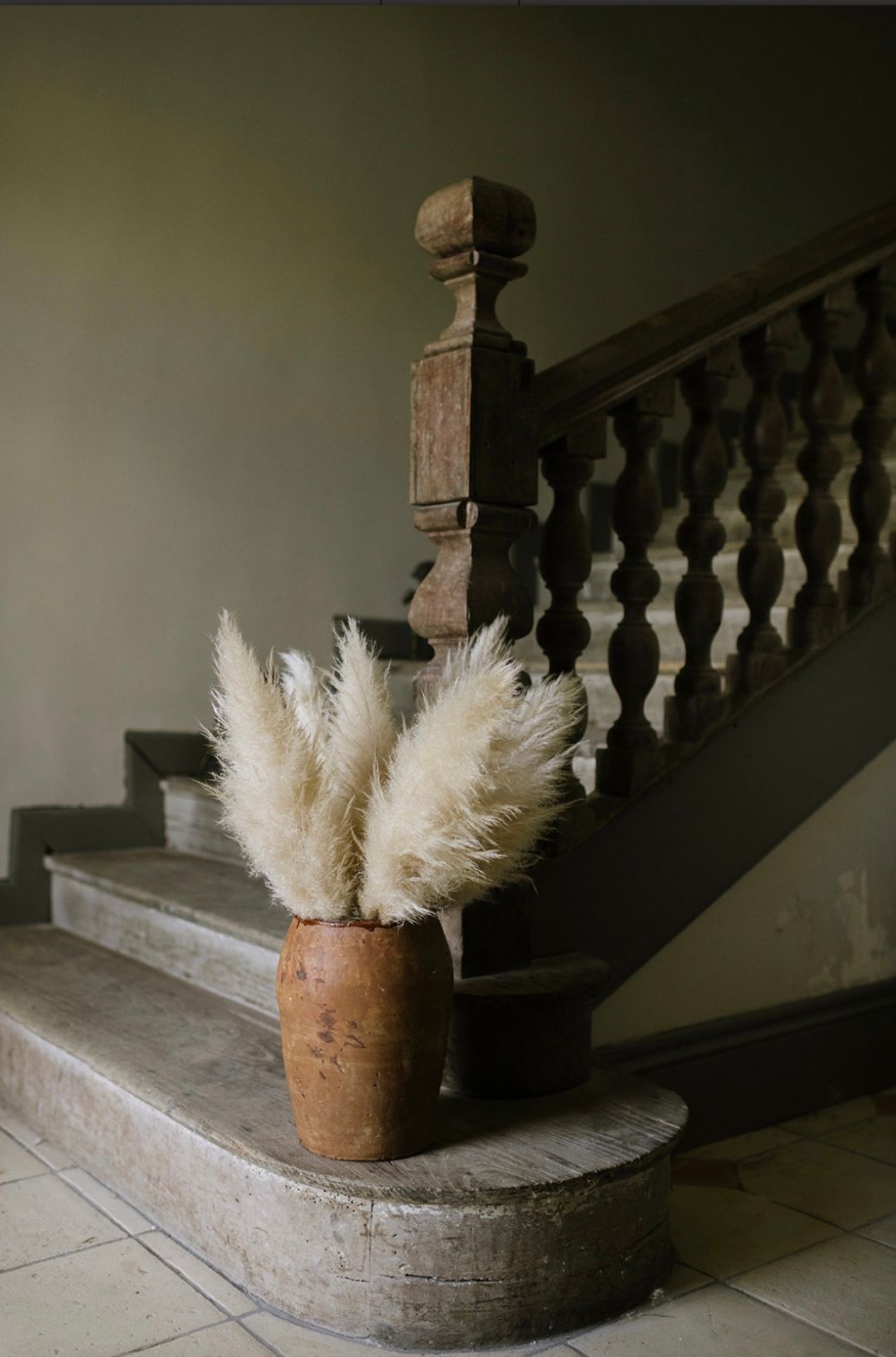 Pampas grass in a terracotta pot sits on a stone staircase landing with dark wooden railings.