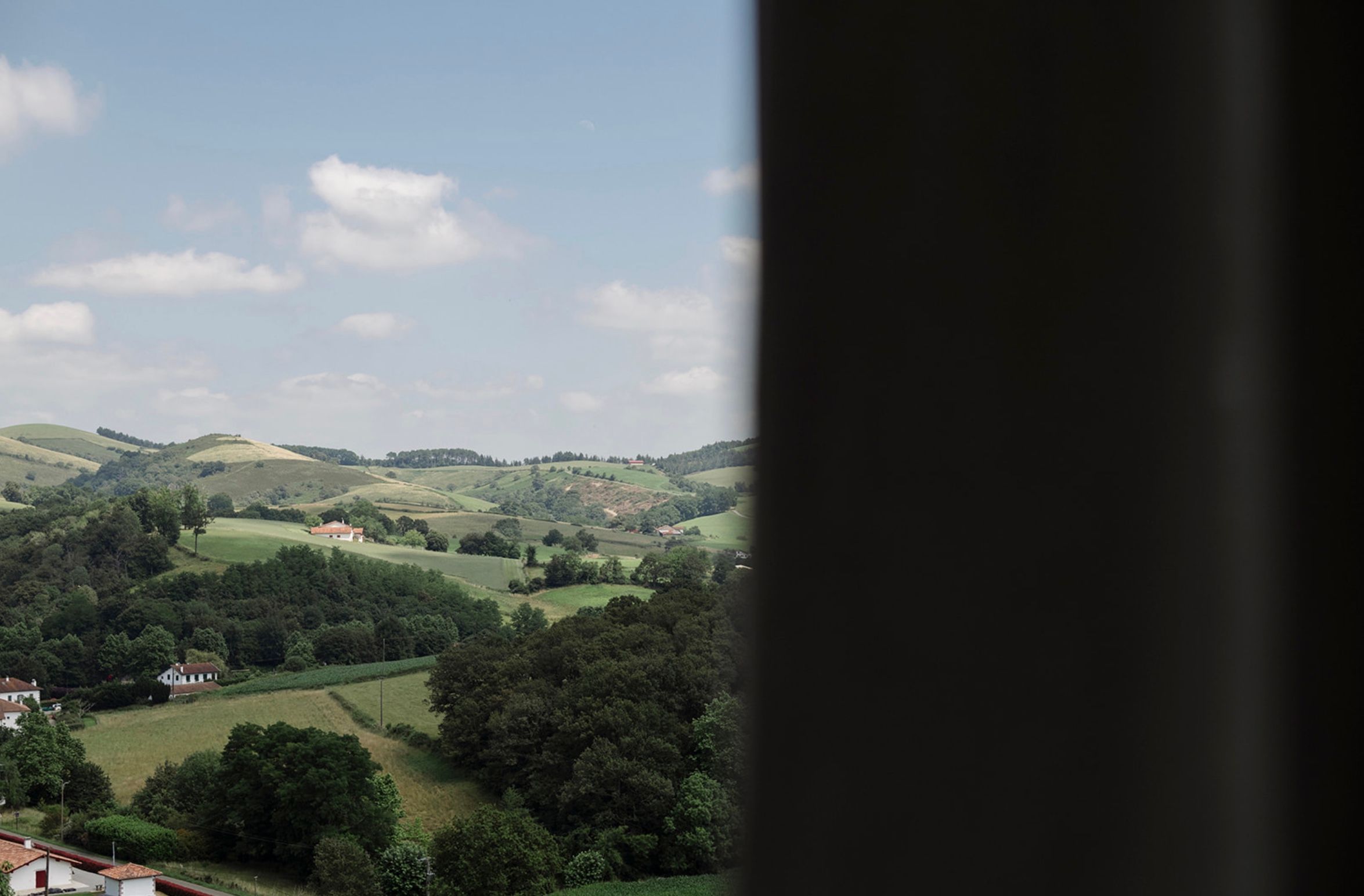 Rolling green hills and mountains stretch across a scenic rural landscape under a cloudy sky.