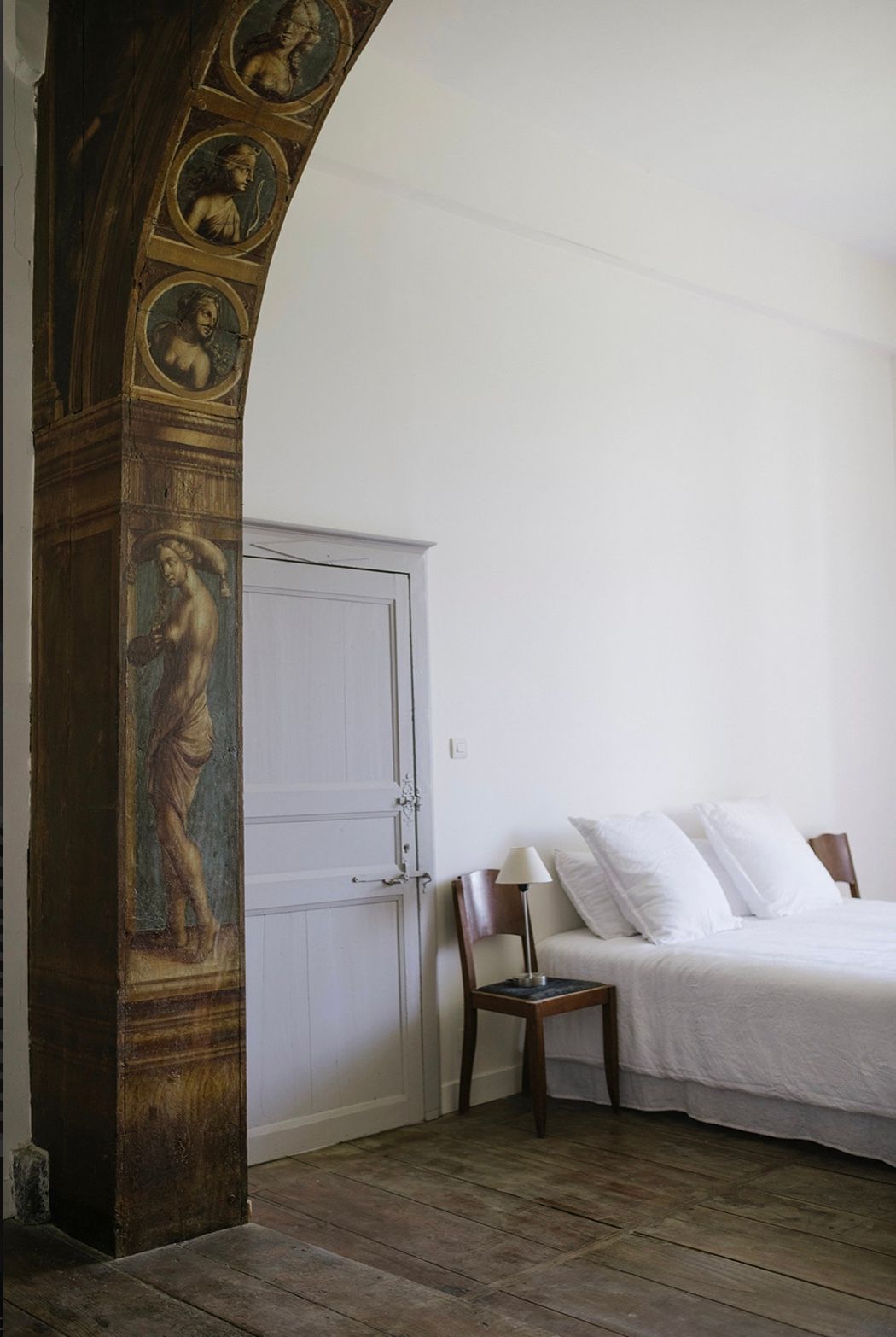 A minimalist bedroom with white bedding and an ornate carved wooden archway featuring decorative panels.