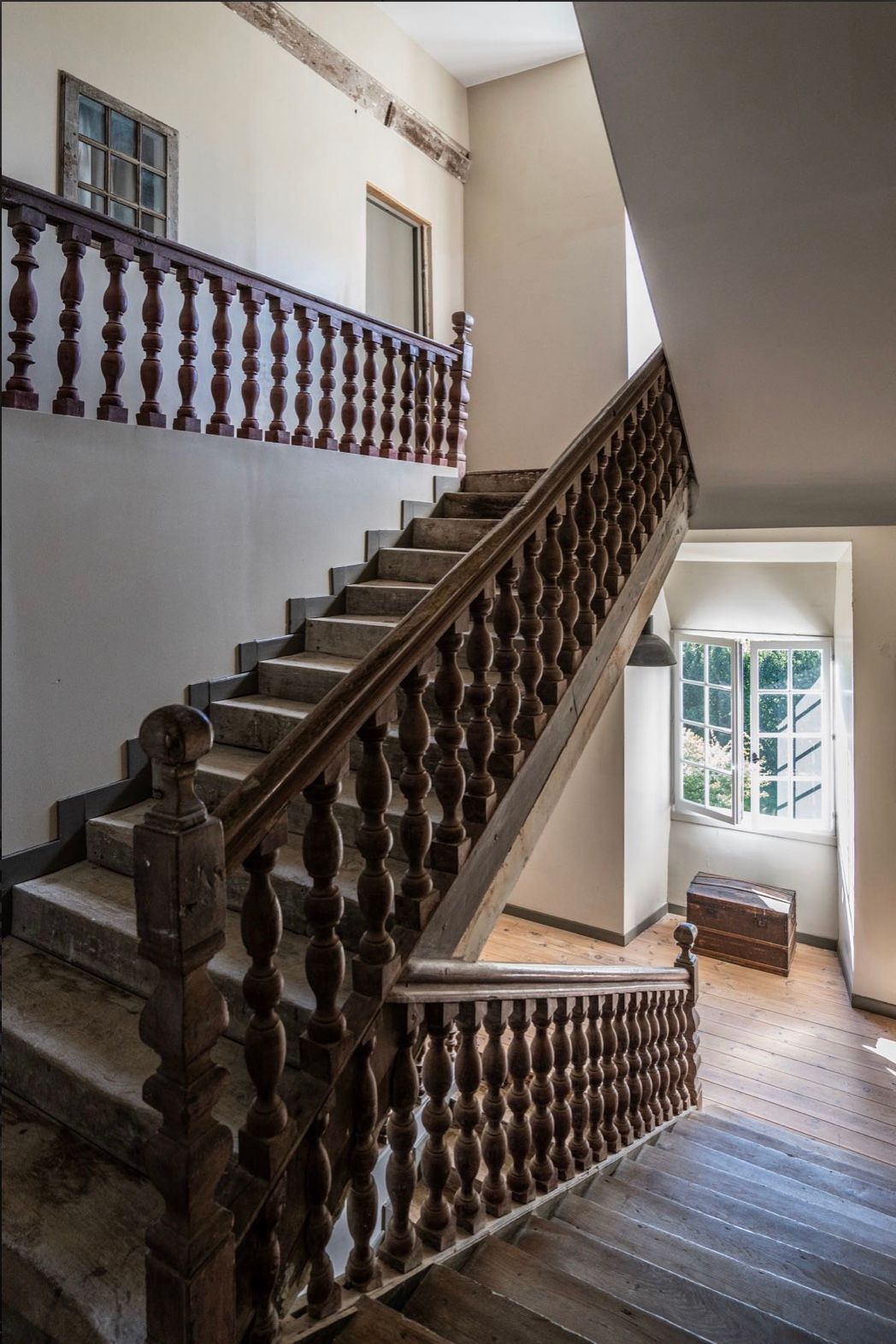 An elegant wooden staircase with ornate balusters and natural light streaming through a window in a historic building.