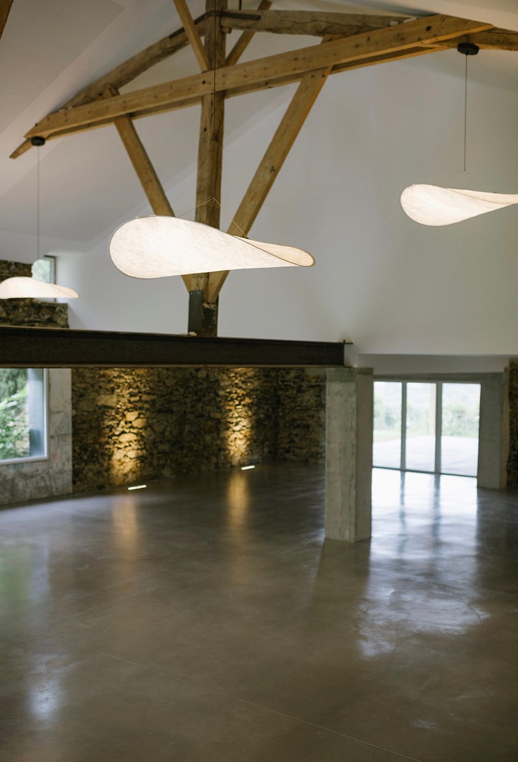 Modern industrial event space with exposed wooden beams, stone walls, and polished concrete floors in an open layout.