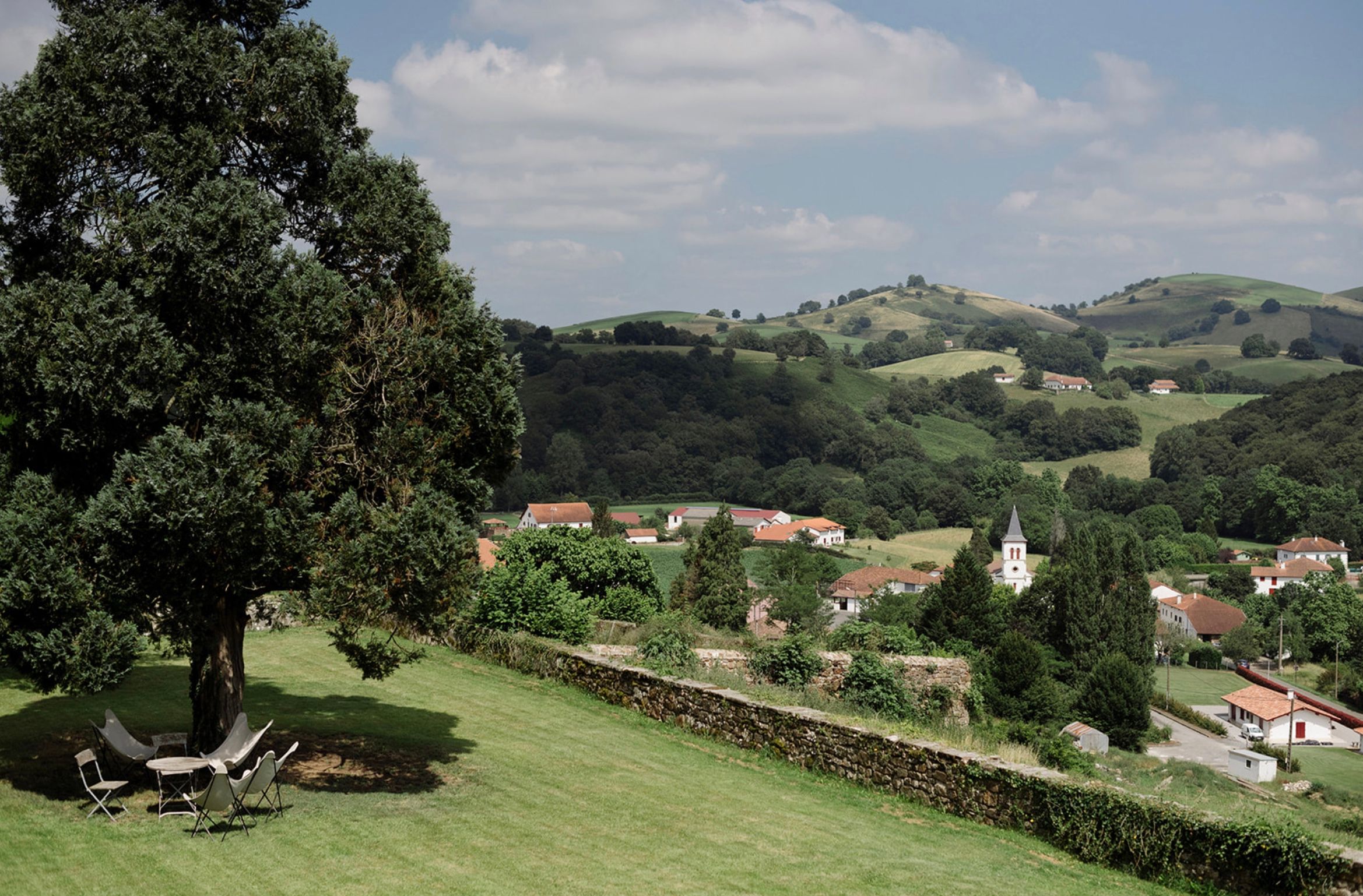 A scenic view of a small village nestled in rolling green hills with a white church spire visible among the buildings.