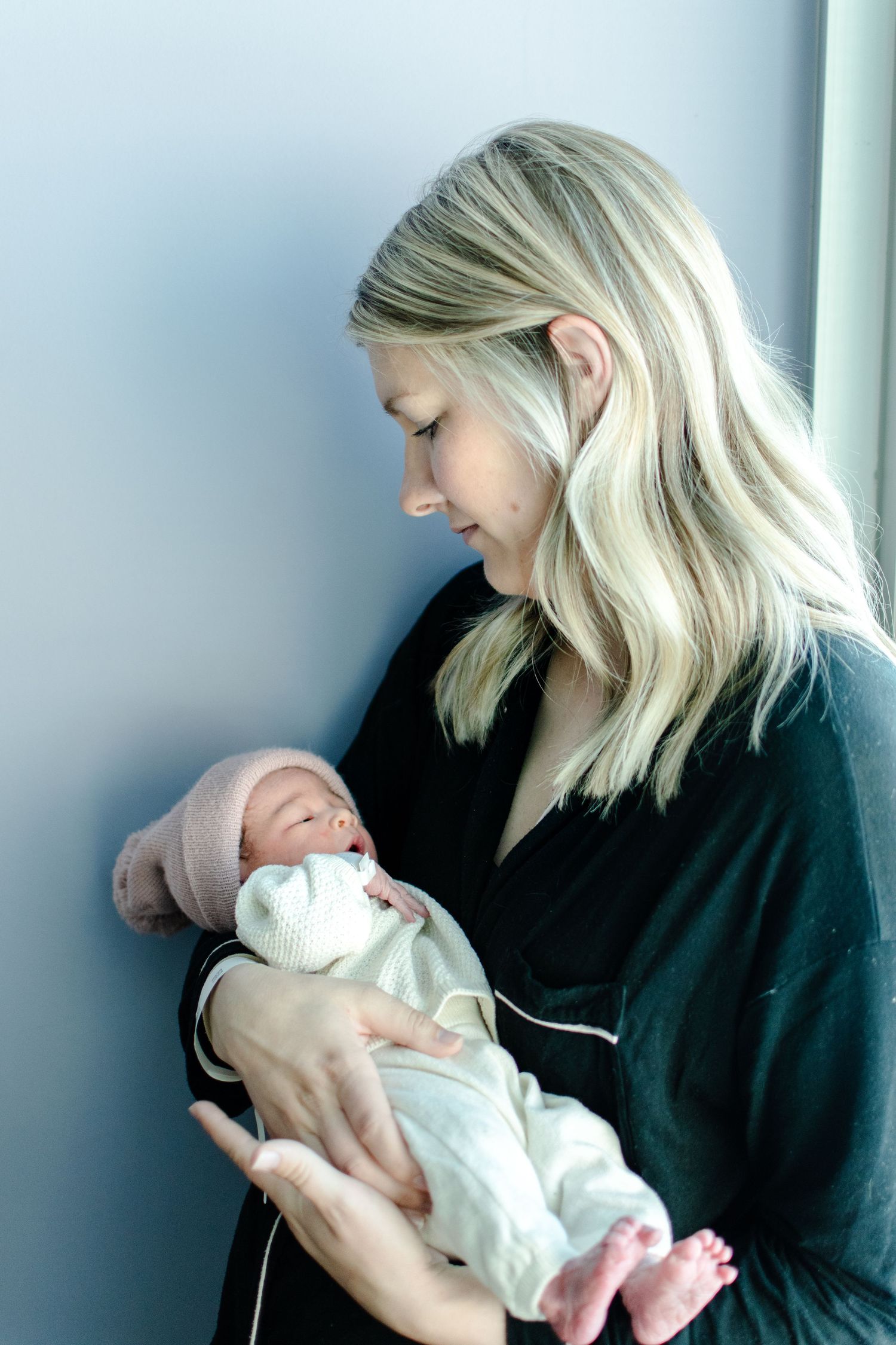 A tender moment between a parent and newborn baby in white swaddle against a blue wall.