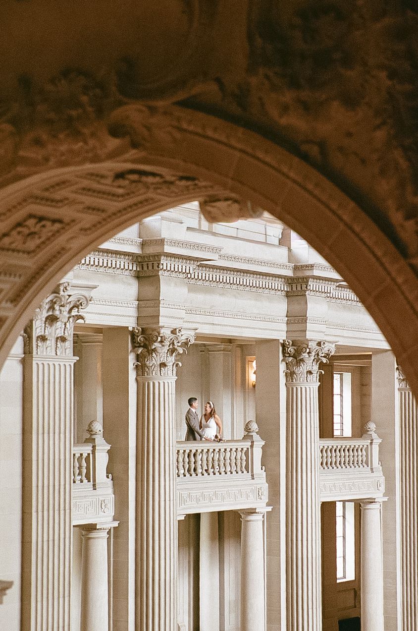 Classical architecture with ornate Corinthian columns and balustrades viewed through an arched entrance in sepia tones.