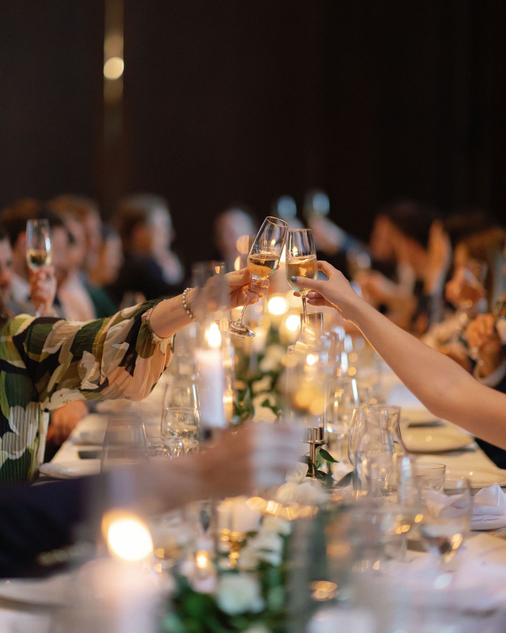 Wedding guests raising wine glasses for a toast at an intimate candlelit reception dinner.