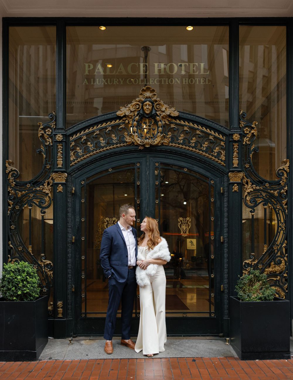 Couple posing in front of ornate Palace Hotel entrance with decorative black archway.