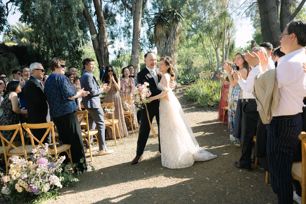 Outdoor wedding ceremony with guests lined up along a tree-lined path.