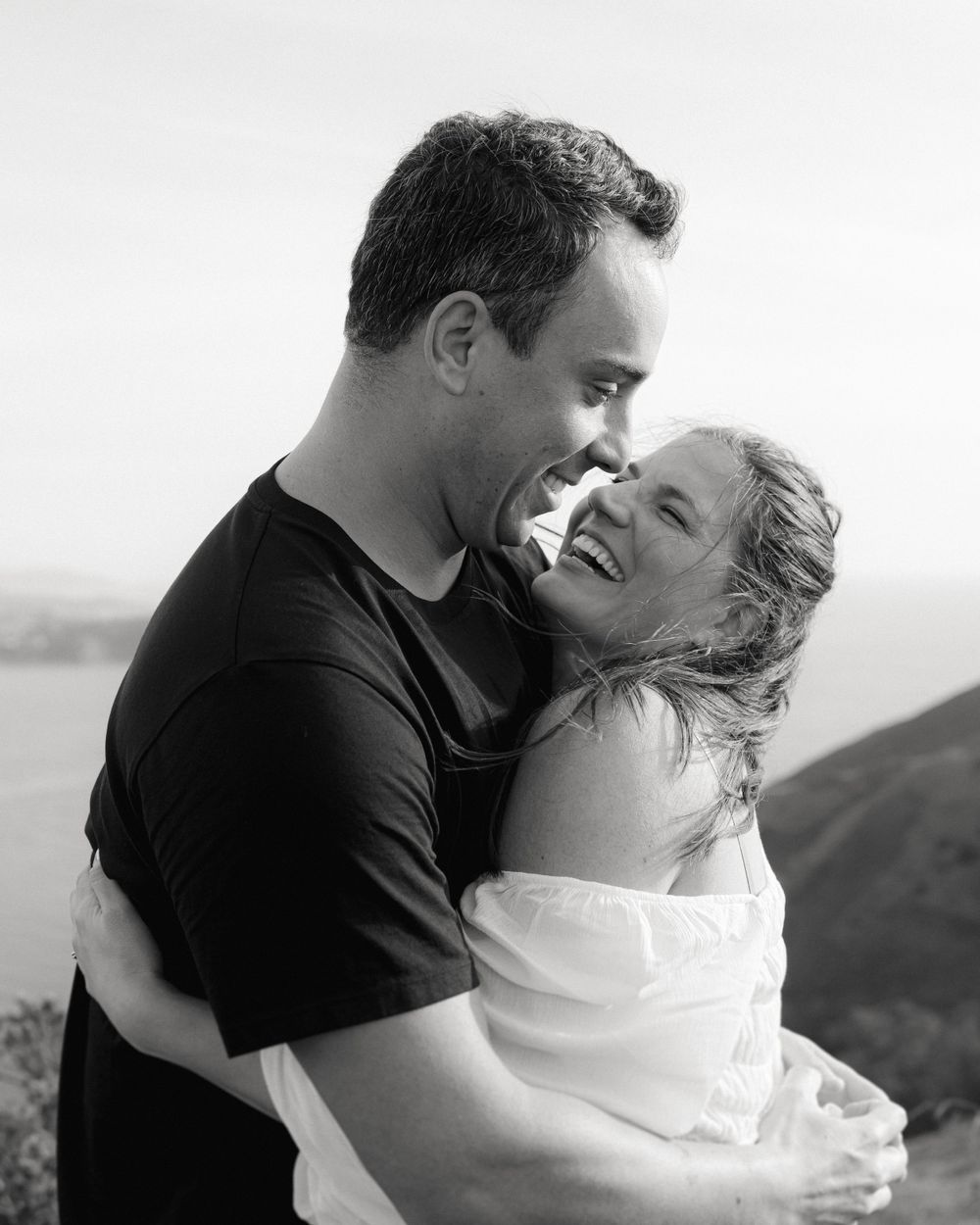 A black and white portrait of a couple sharing a tender moment outdoors.