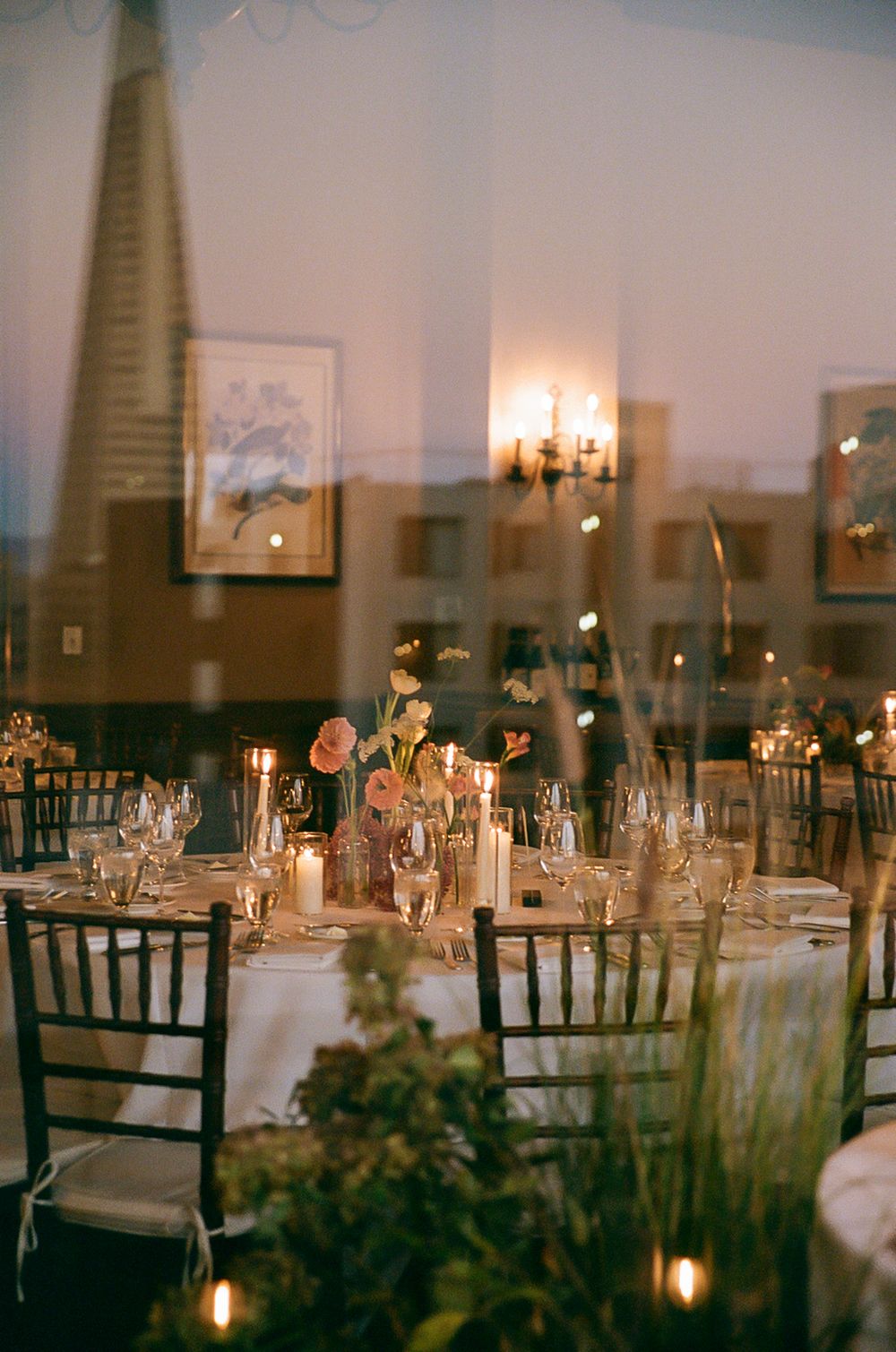 Elegant wedding reception tables set with white linens, candles and floral centerpieces in a dimly lit banquet room.