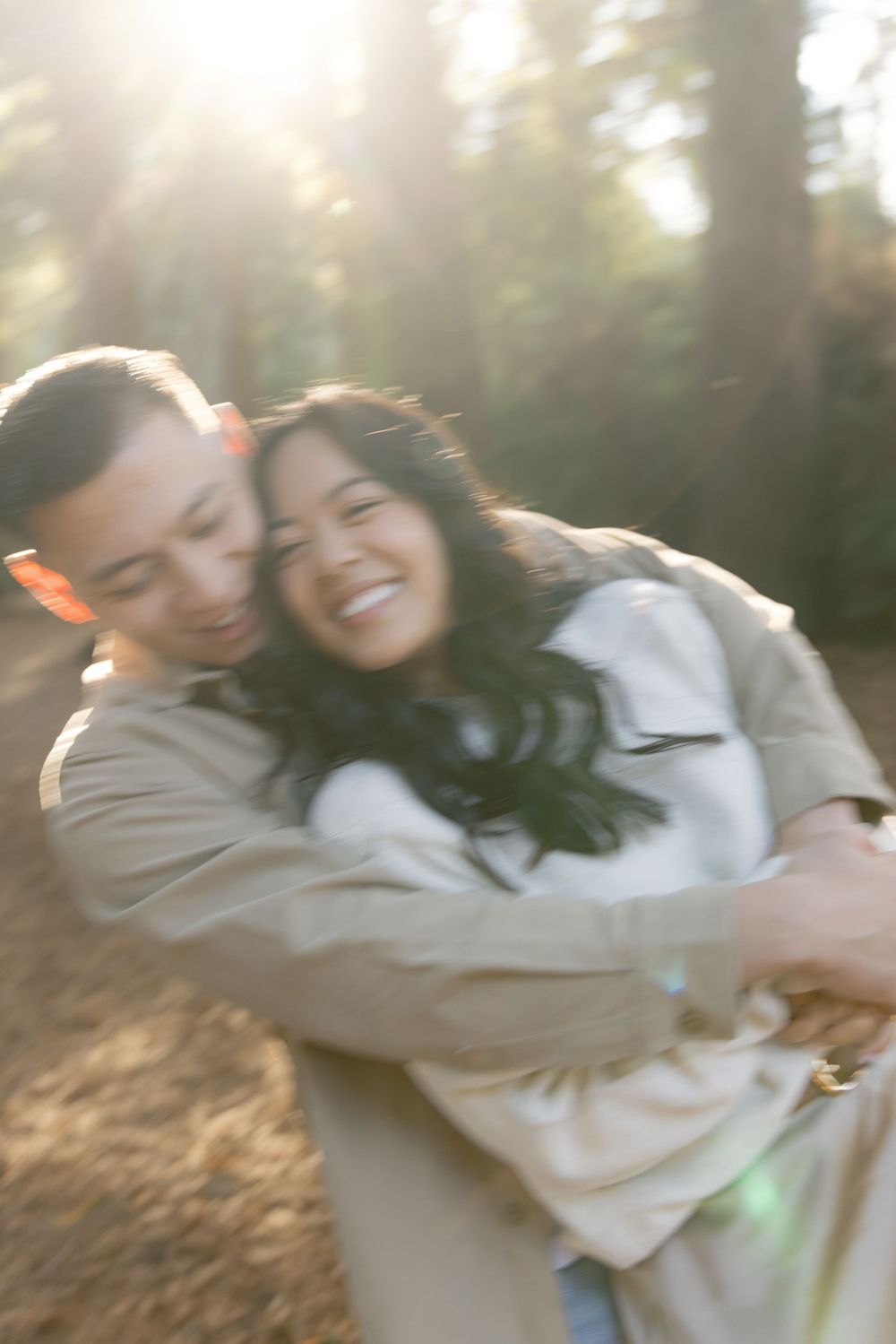 Couple sharing a candid laughing embrace during a sunlit outdoor photoshoot.
