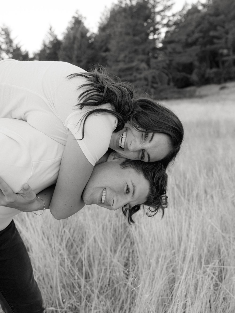 Black and white portrait of couple embracing in tall grass field.