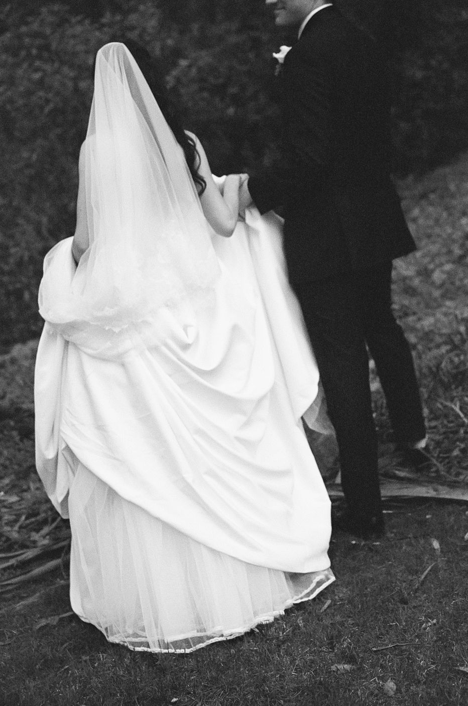 A black and white wedding photo series showing the flowing movement of a white bridal gown and veil against dark scenery.