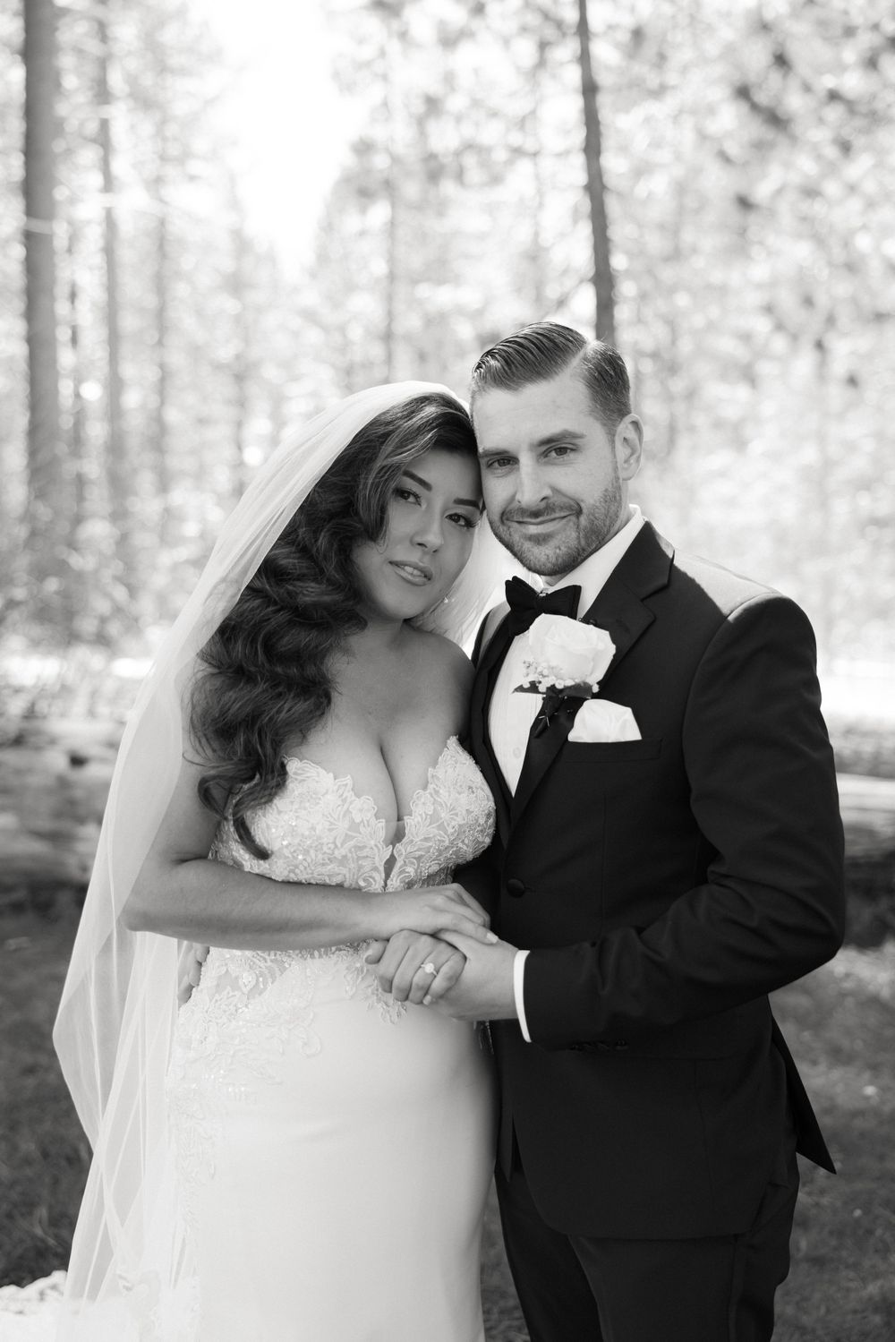 A black and white portrait of a bride and groom posing together in a forest setting.