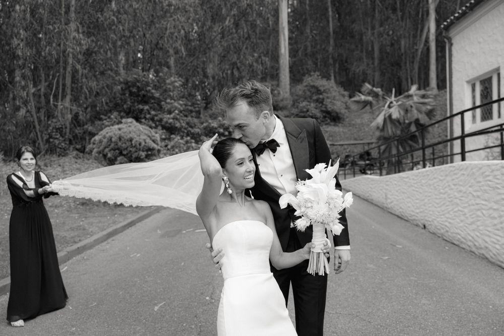 Black and white wedding portrait on a tree-lined path with classic formal attire.