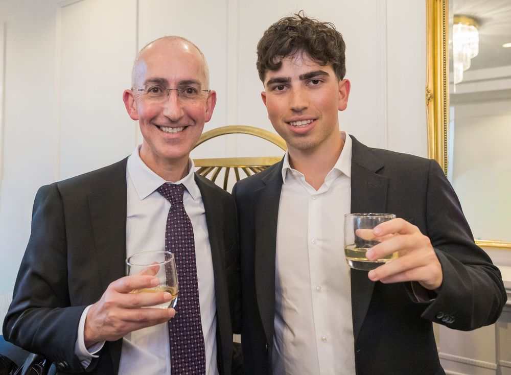 Business professionals in suits smile and raise glasses in celebration at an office gathering.