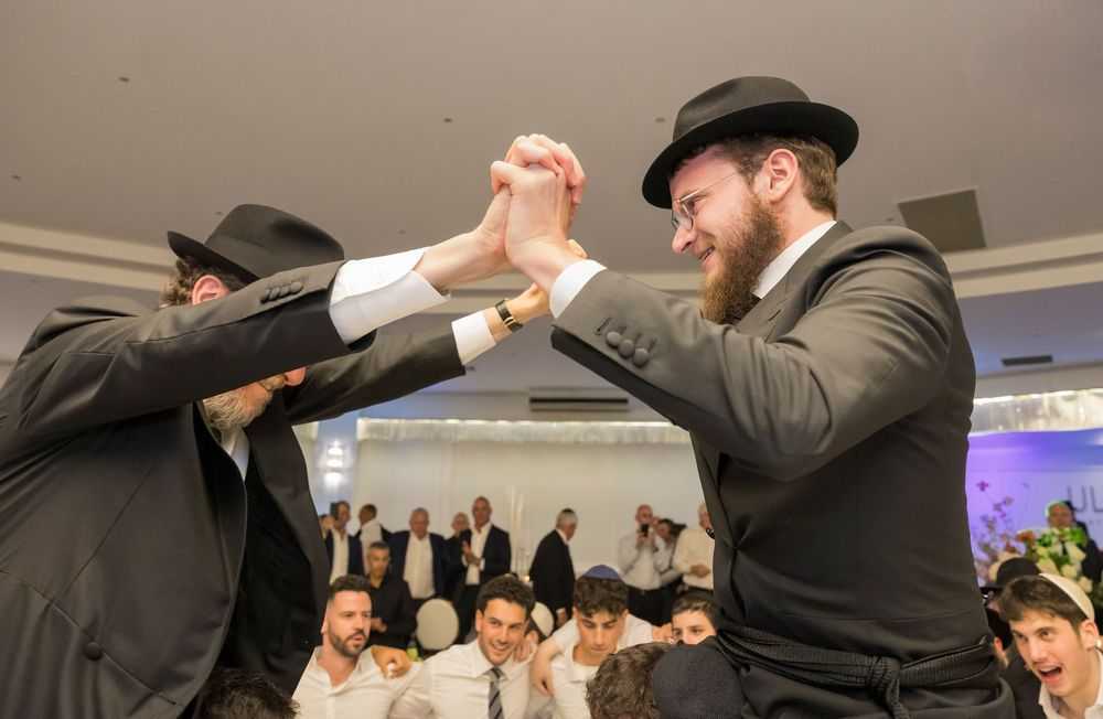 A joyous celebration at a Jewish wedding ceremony with people dancing and embracing in traditional attire.