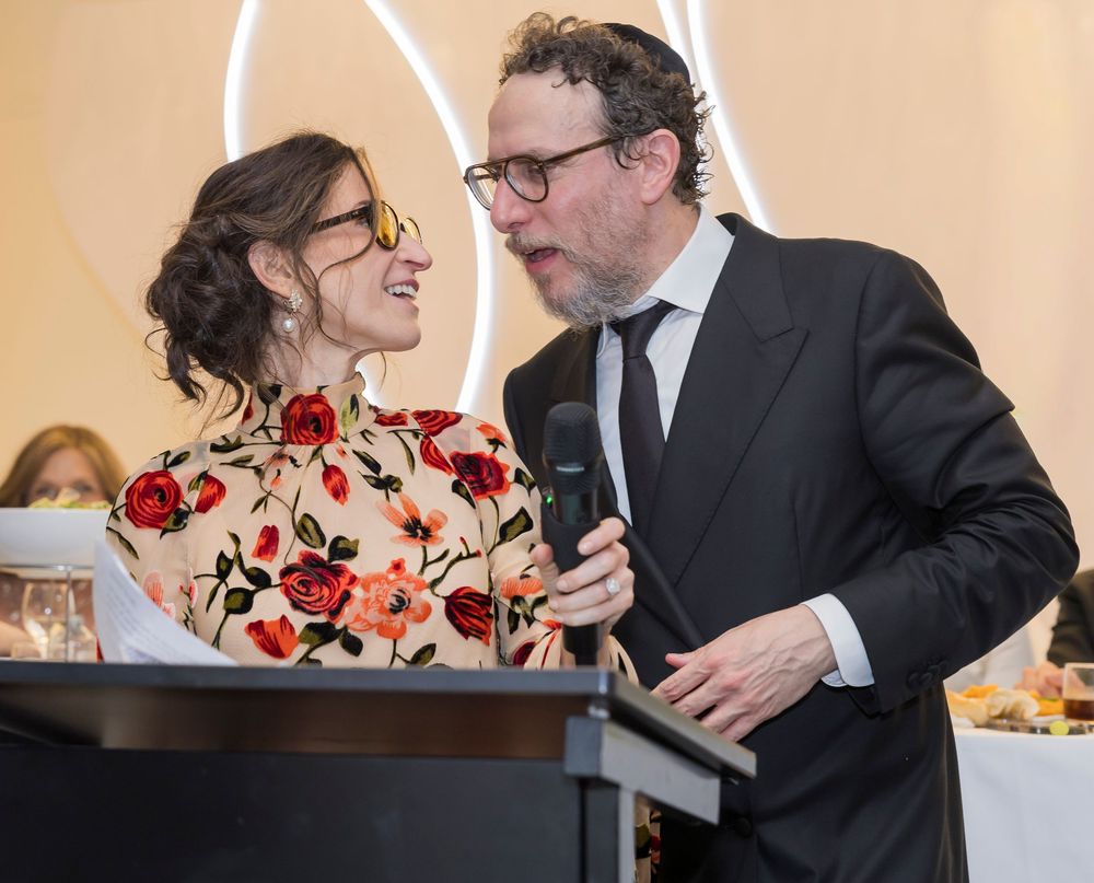 A couple in formal attire shares a romantic moment, with the woman wearing a floral dress and the man in a dark suit.