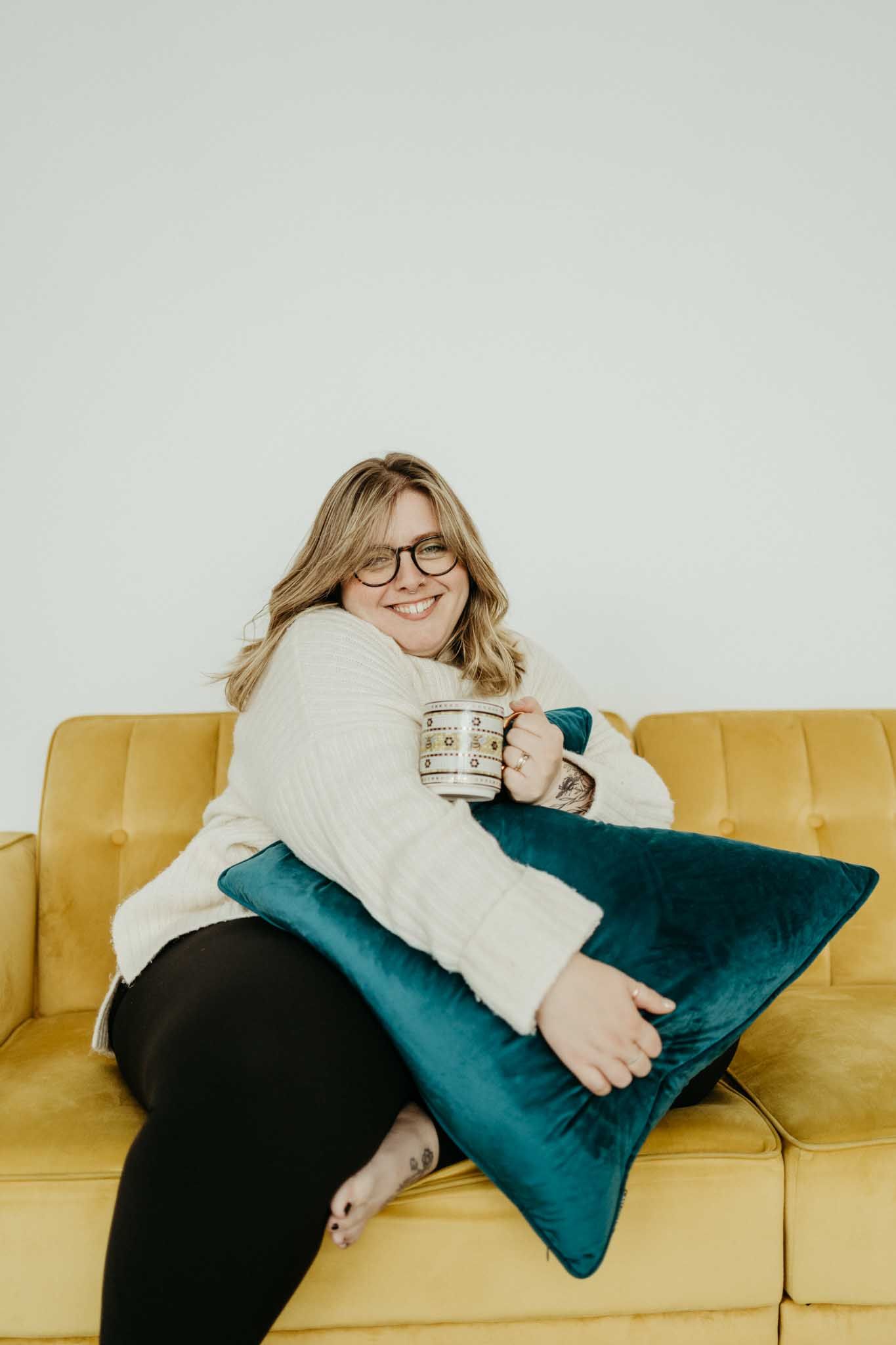Casual portrait of person relaxing on yellow couch with teal pillow and coffee mug.