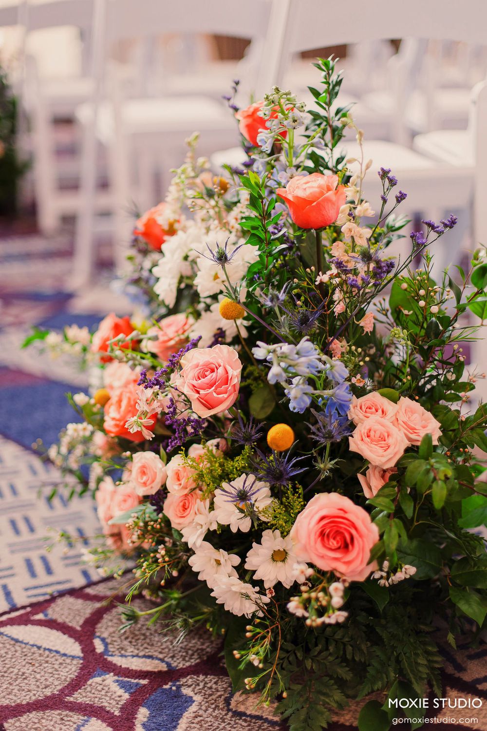 Elegant floral centerpieces featuring pink roses, white daisies, and purple blooms arranged on a blue and white patterned tablecloth.