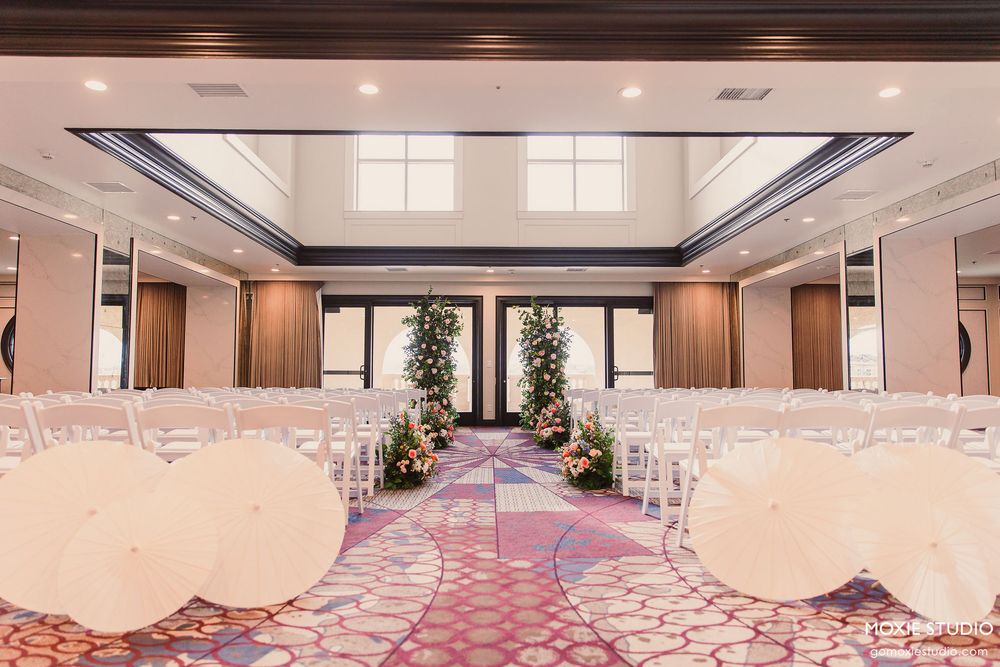 Elegant ballroom interior with pink carpeting, crystal chandeliers, and curved architectural details illuminated by warm lighting.