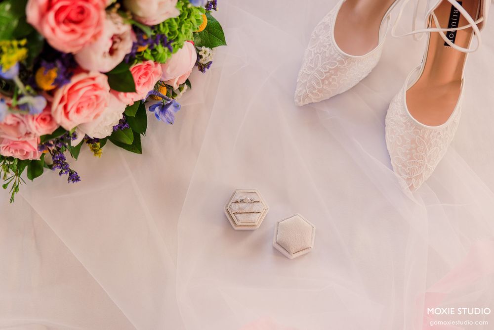 Elegant bridal shoes surrounded by pink roses and delicate flowers on a soft pink background.