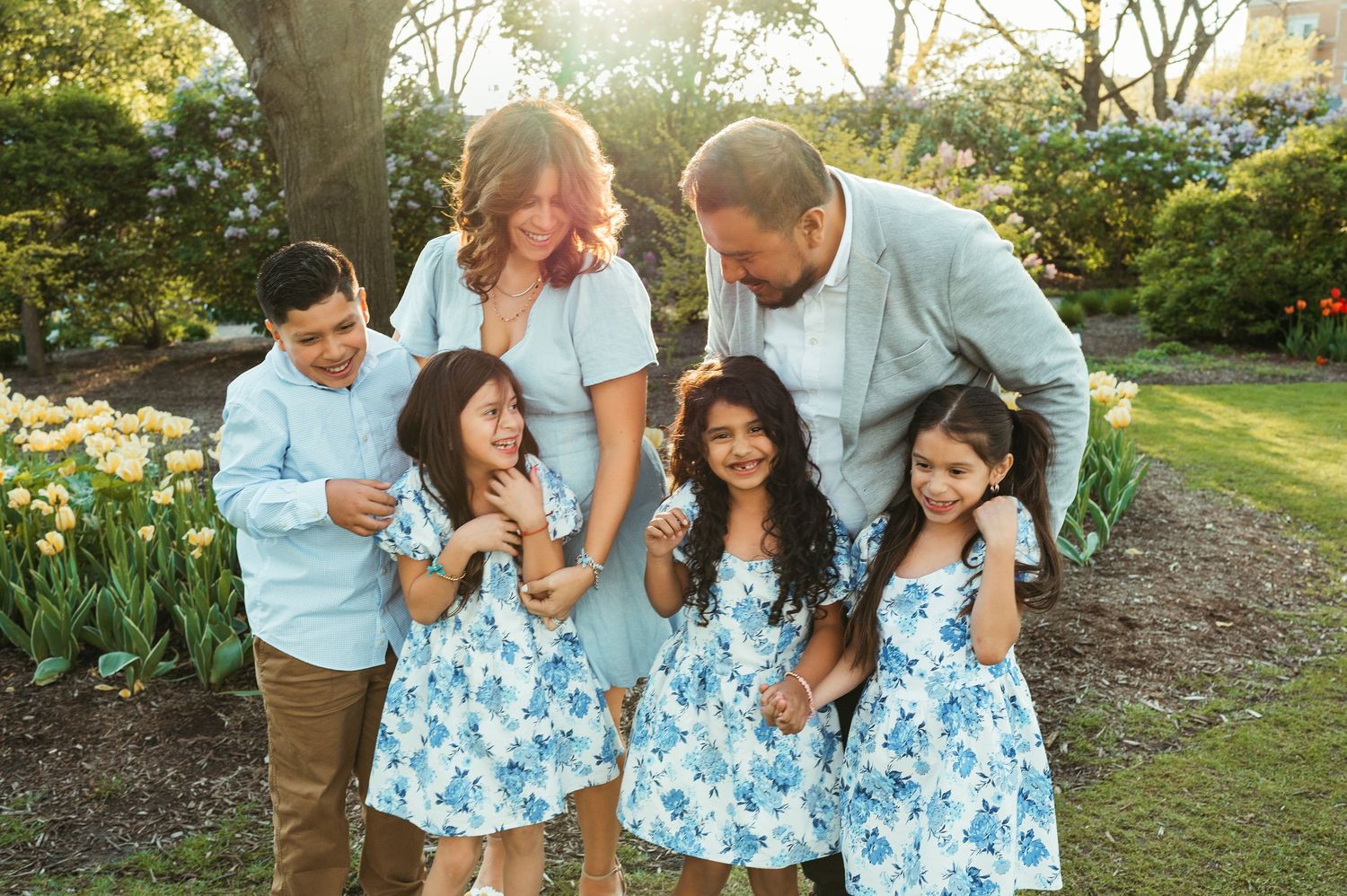Family of six in matching blue floral outfits laughing together in spring garden with tulips.