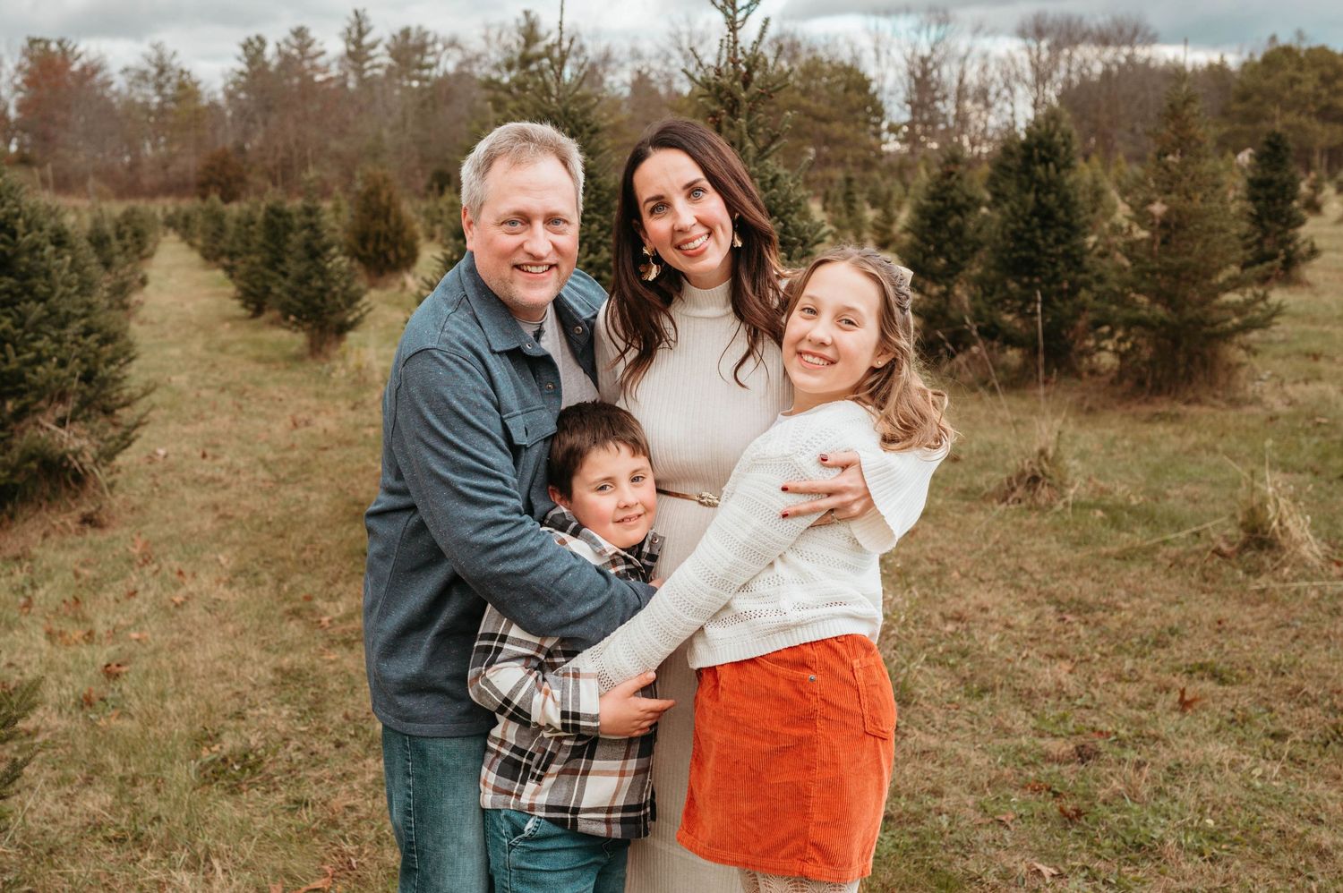 Family of four posing together at Christmas tree farm.