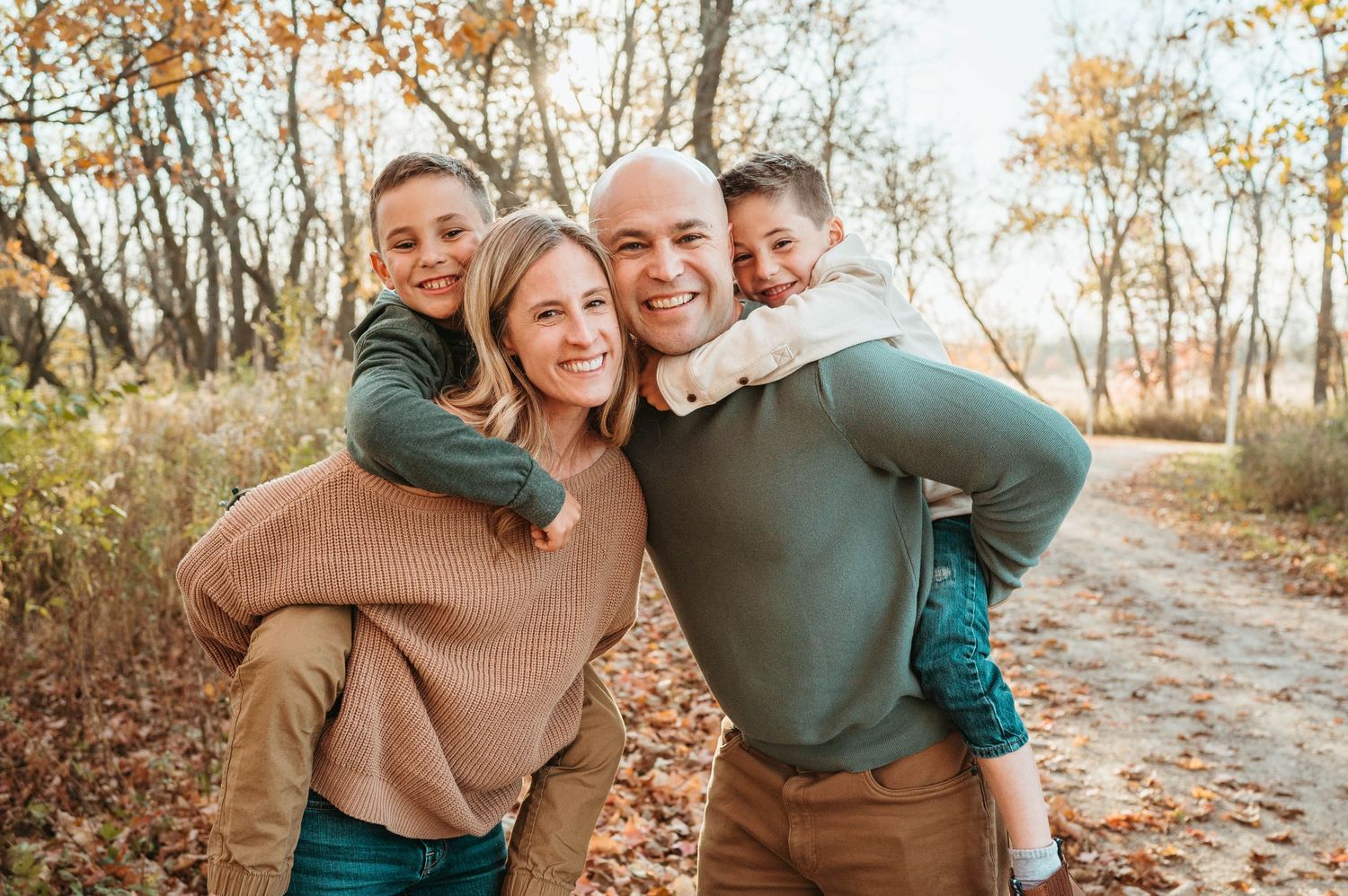 Smiling family of four in autumn woods with kids on parents backs.