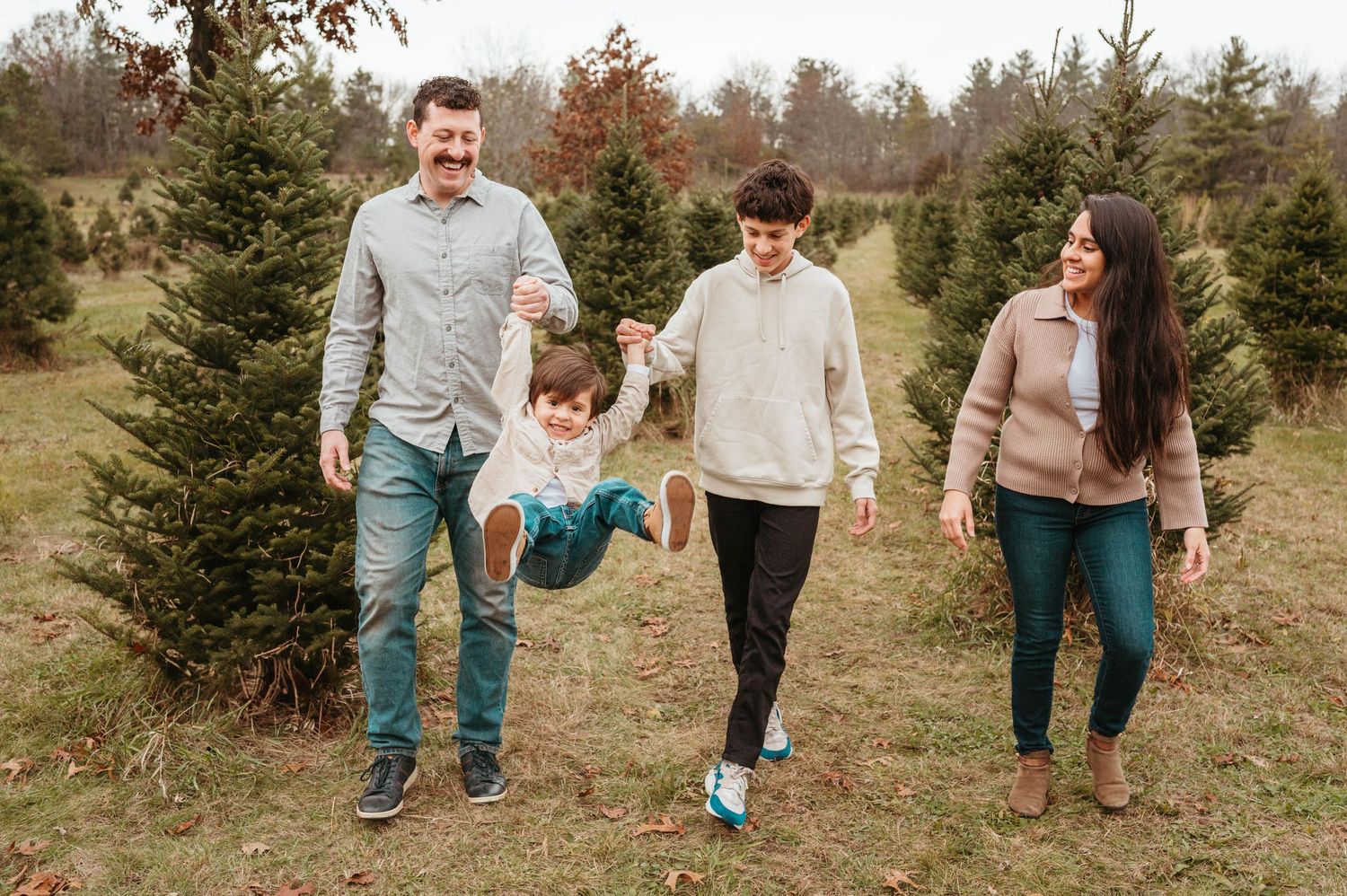 Family of four swinging toddler between parents at a Christmas tree farm.