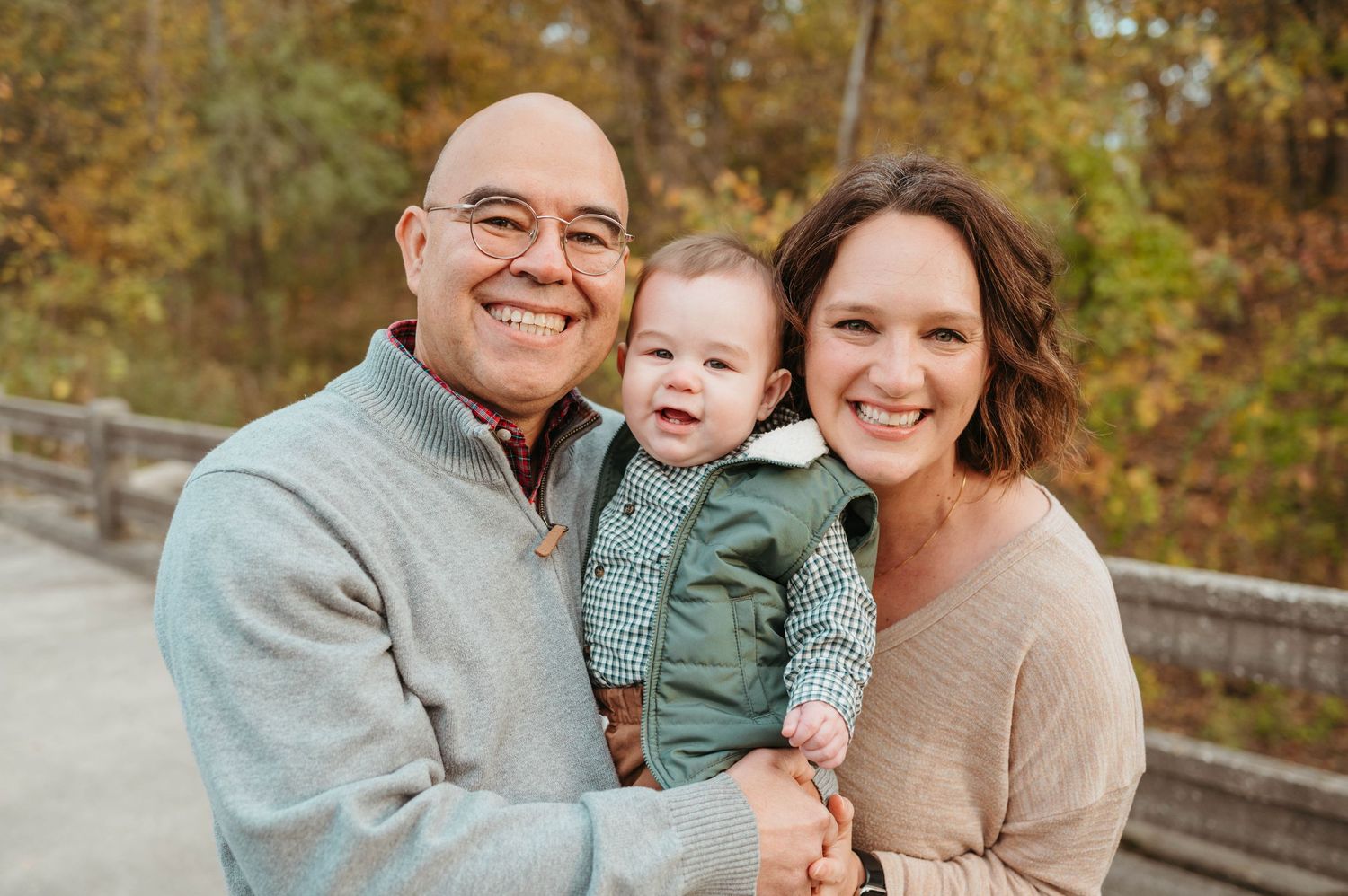 Smiling couple with happy baby outdoors in fall setting.