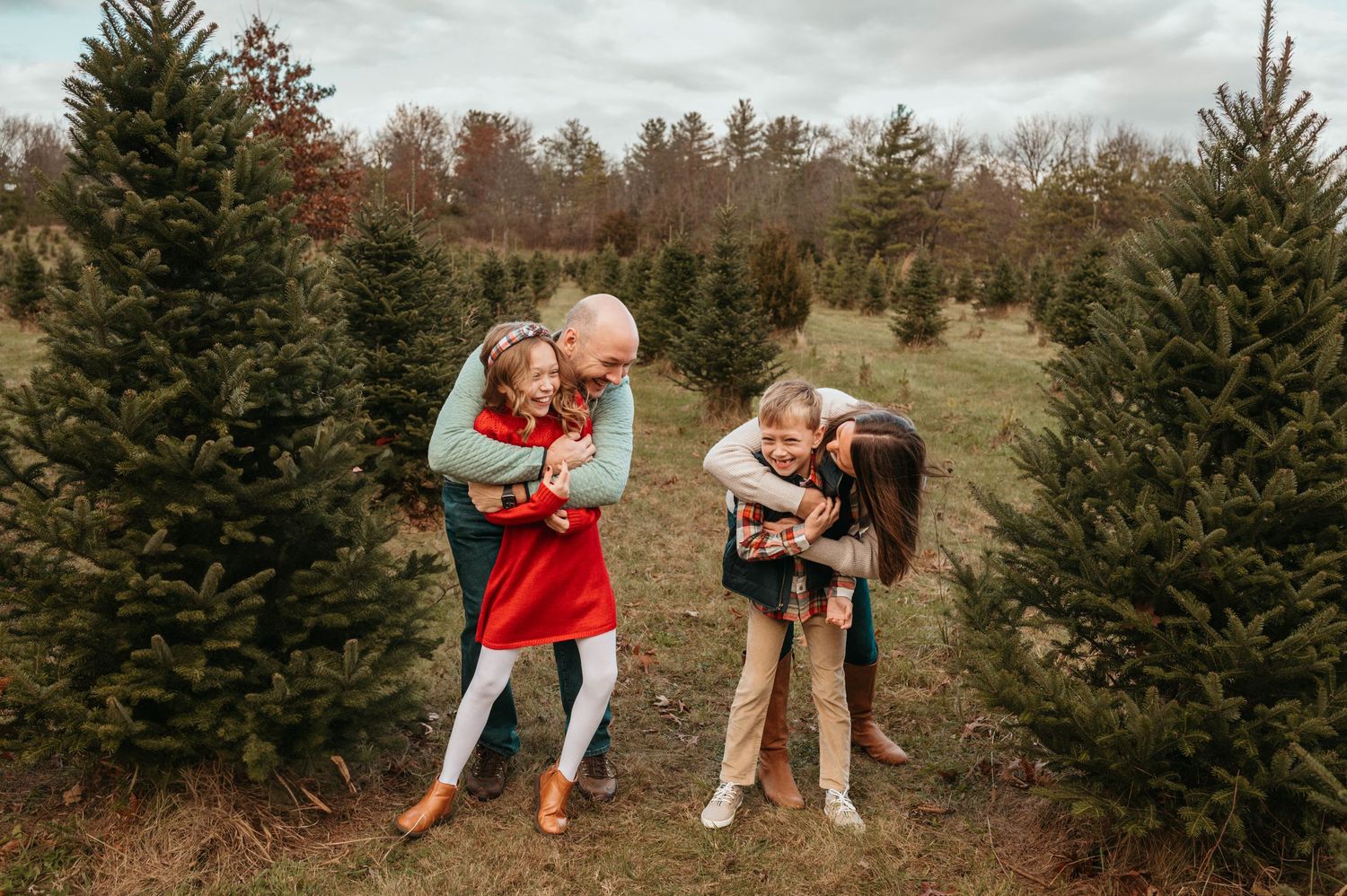 Family with two kids at Christmas tree farm in festive outfits.