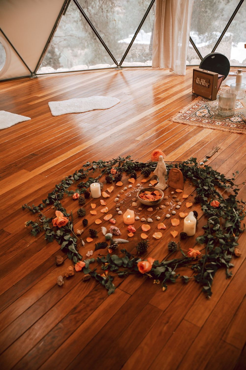Rustic wooden floor decorated with scattered candles, roses, and eucalyptus leaves in a circular pattern.